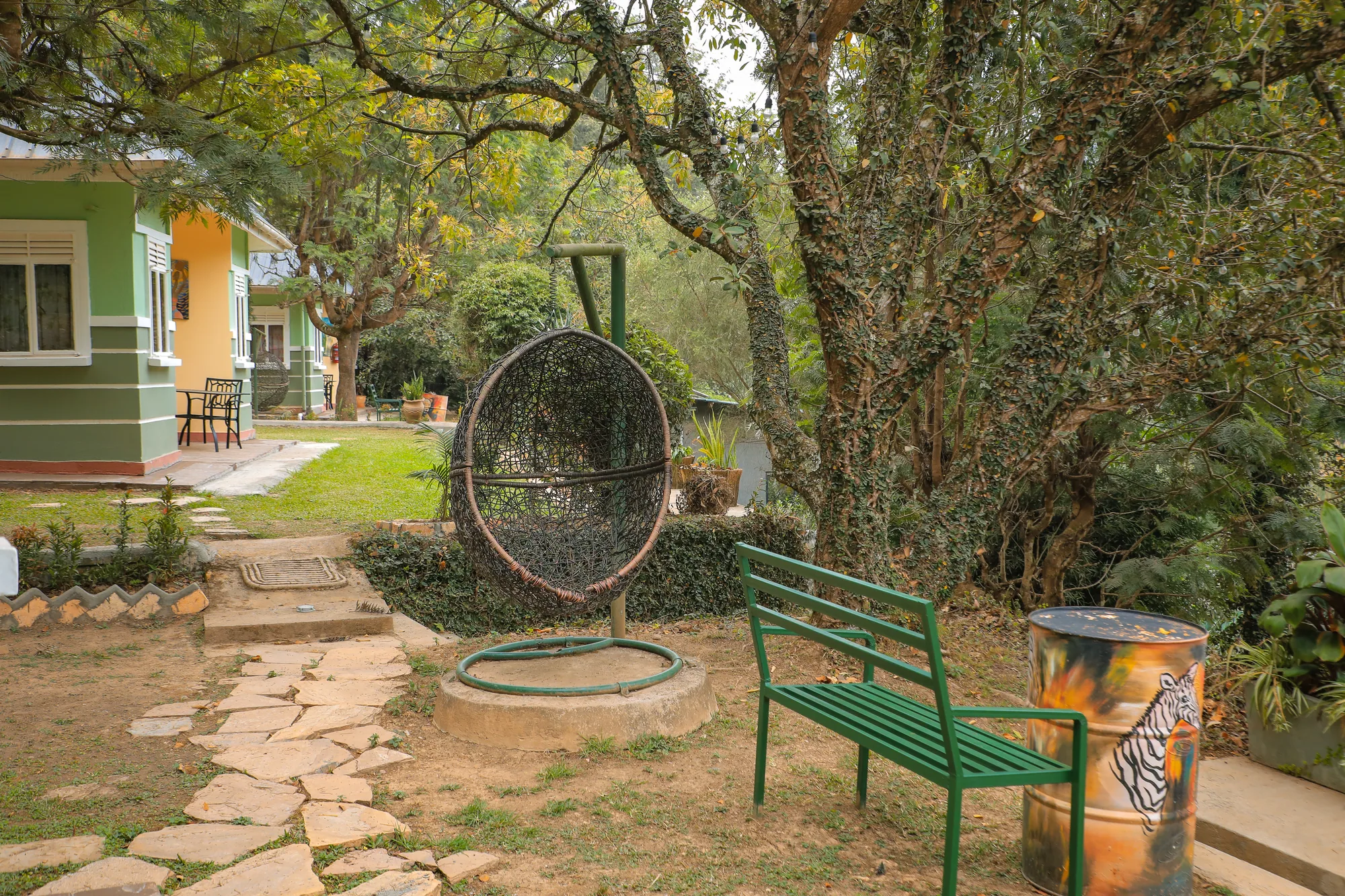 A hanging round swing seat and a green bench on a stone path between the cottages and mature trees
