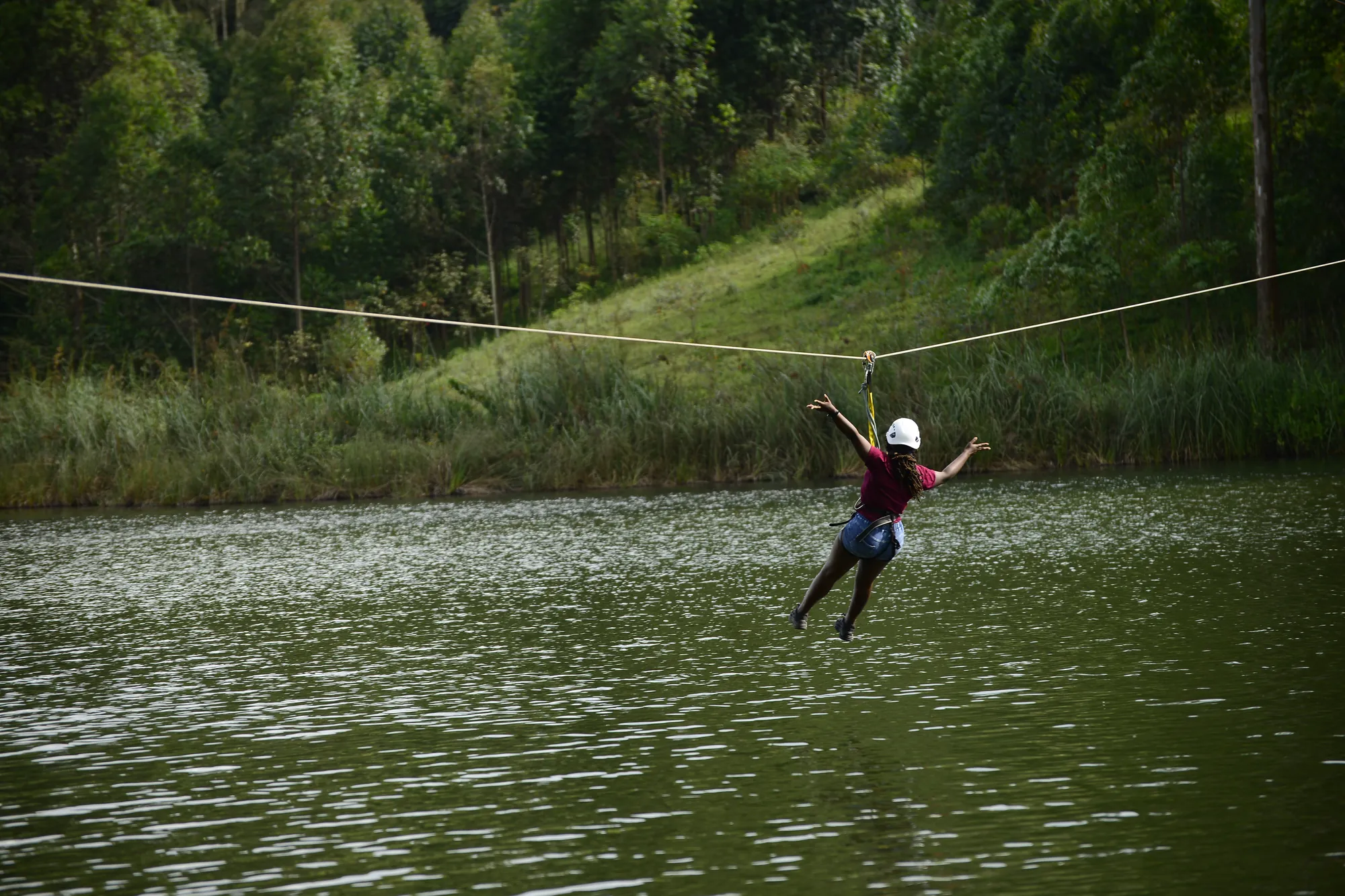 A zip-line rider in a helmet gliding out over the green water of Lake Bunyonyi