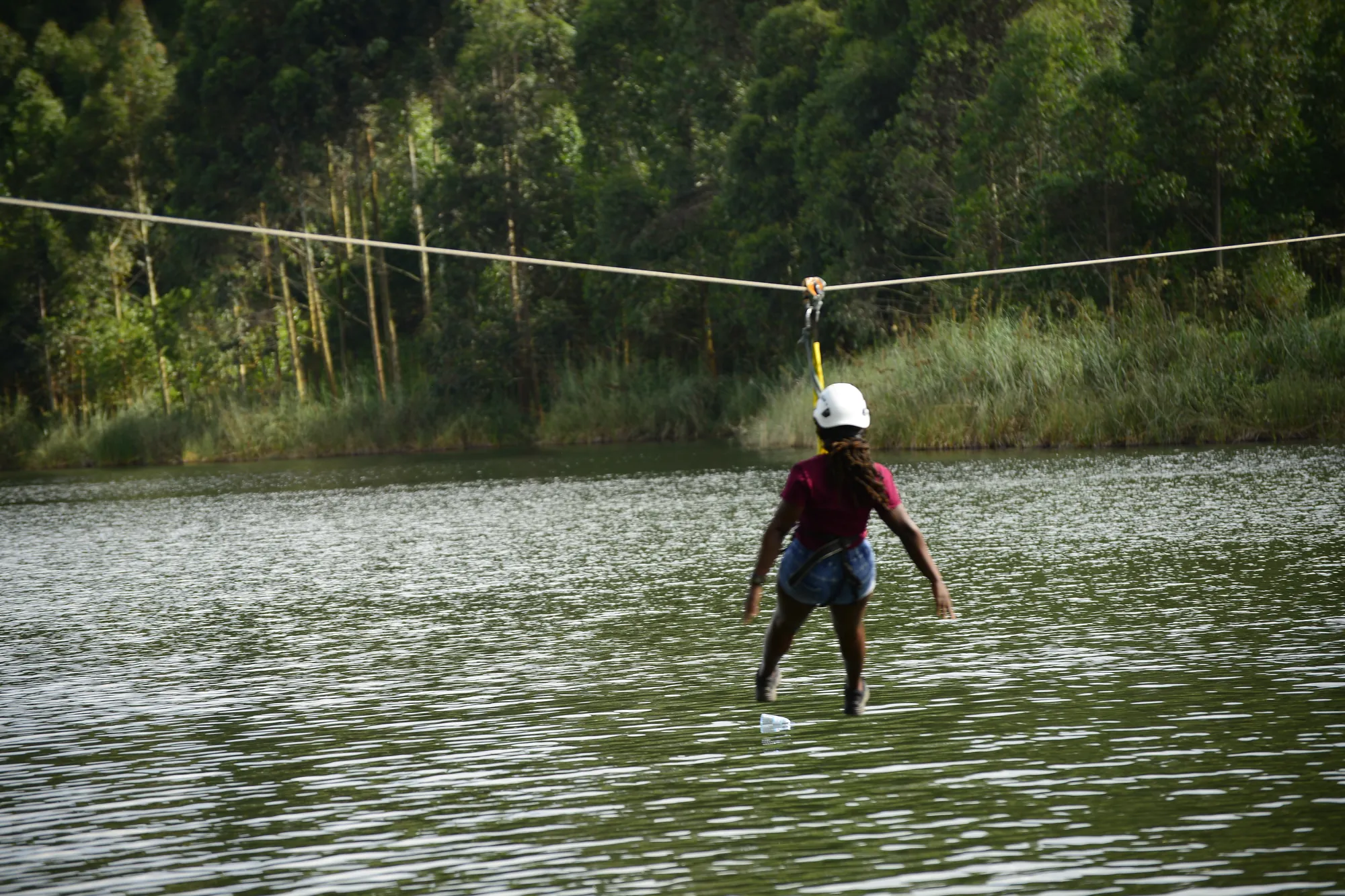 A zip-line rider crossing the middle of the lake channel with the cable stretched above