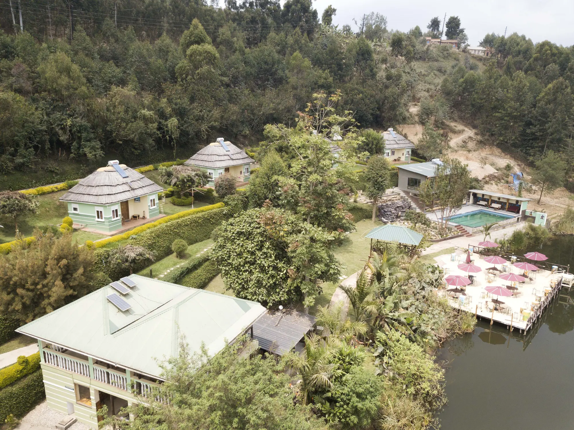 Aerial view of the thatched cottages, main building and pool terrace among trees on the lake shore