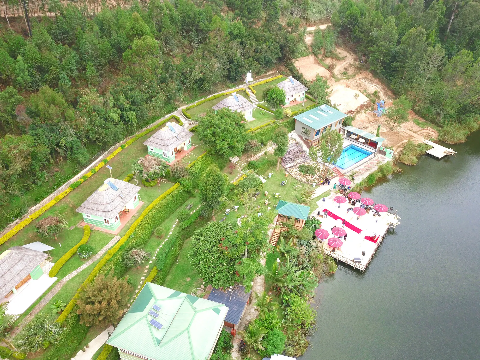Aerial view along the shoreline showing the pool, decks and pink parasols at the water's edge