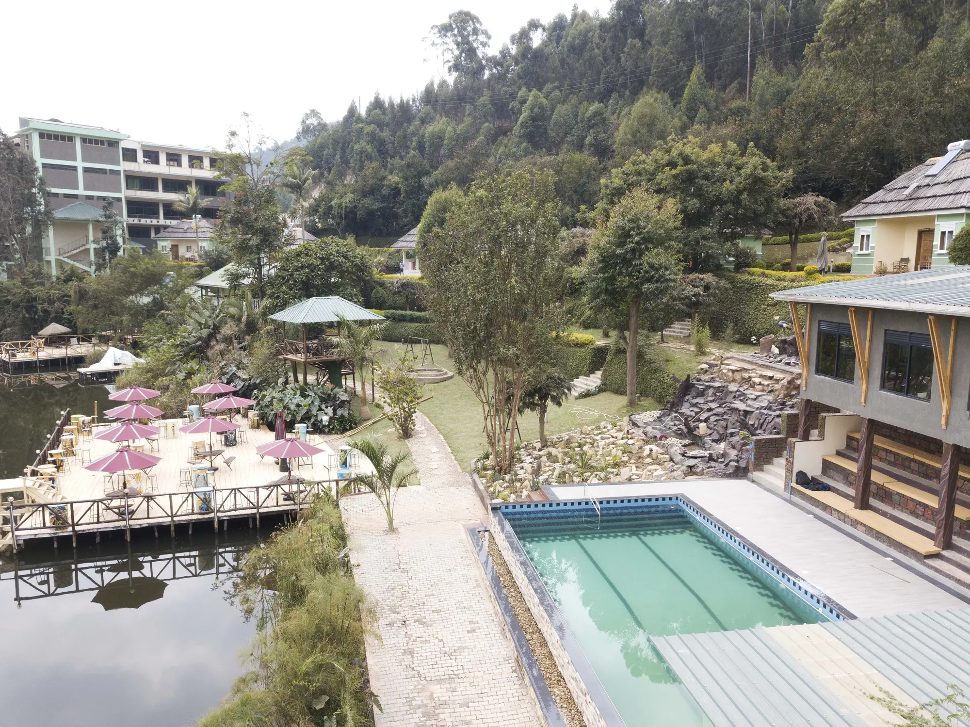 Aerial view of the pool, gazebo walkway and hotel block with forested hills behind