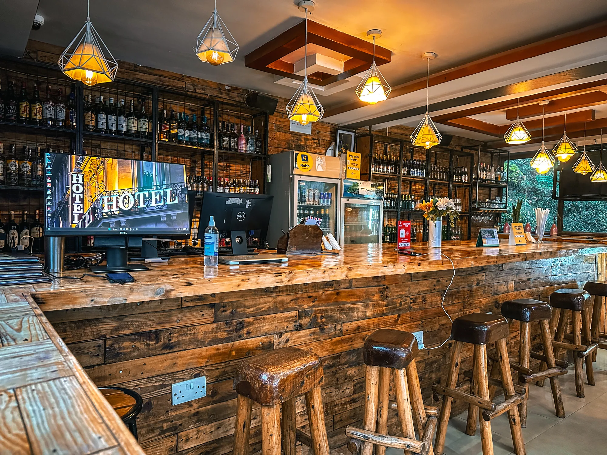 The main bar with a reclaimed timber counter, bottle shelves and pendant lights, stools along the front