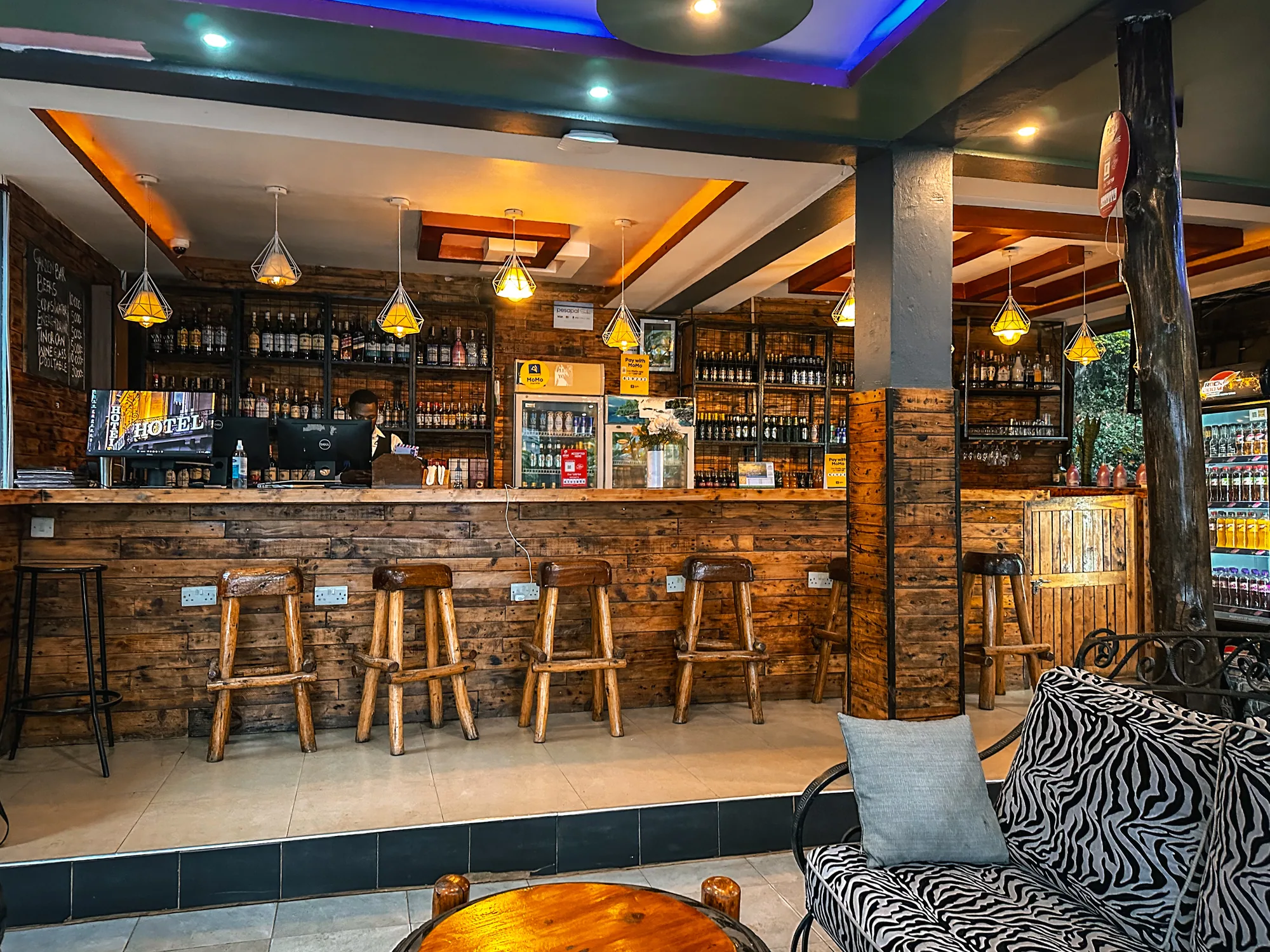 The bar seen from the lounge side, with bar stools, patterned cushions and blue ceiling lighting