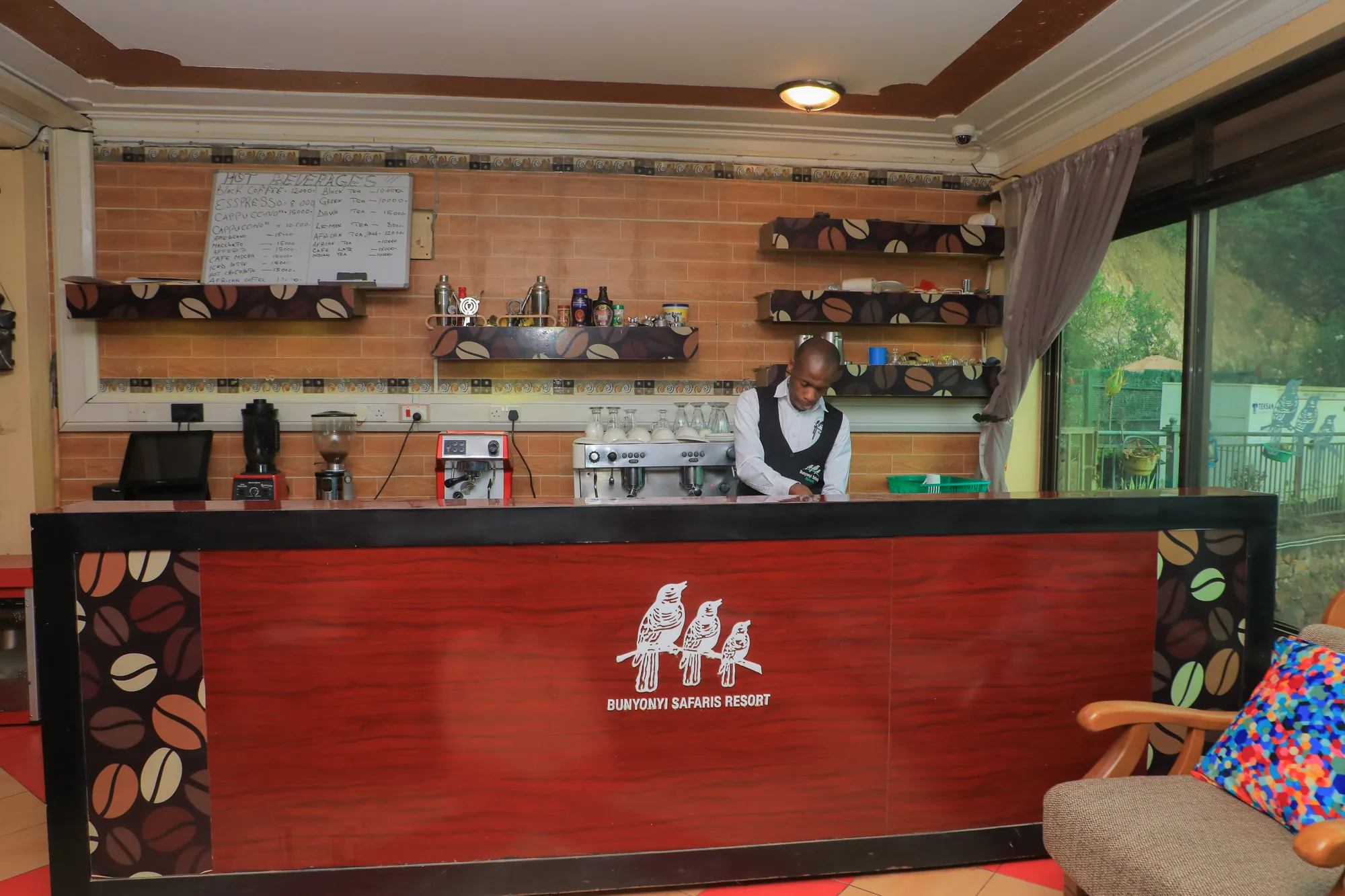 A staff member behind the red coffee-bean-painted coffee counter under a chalk menu board