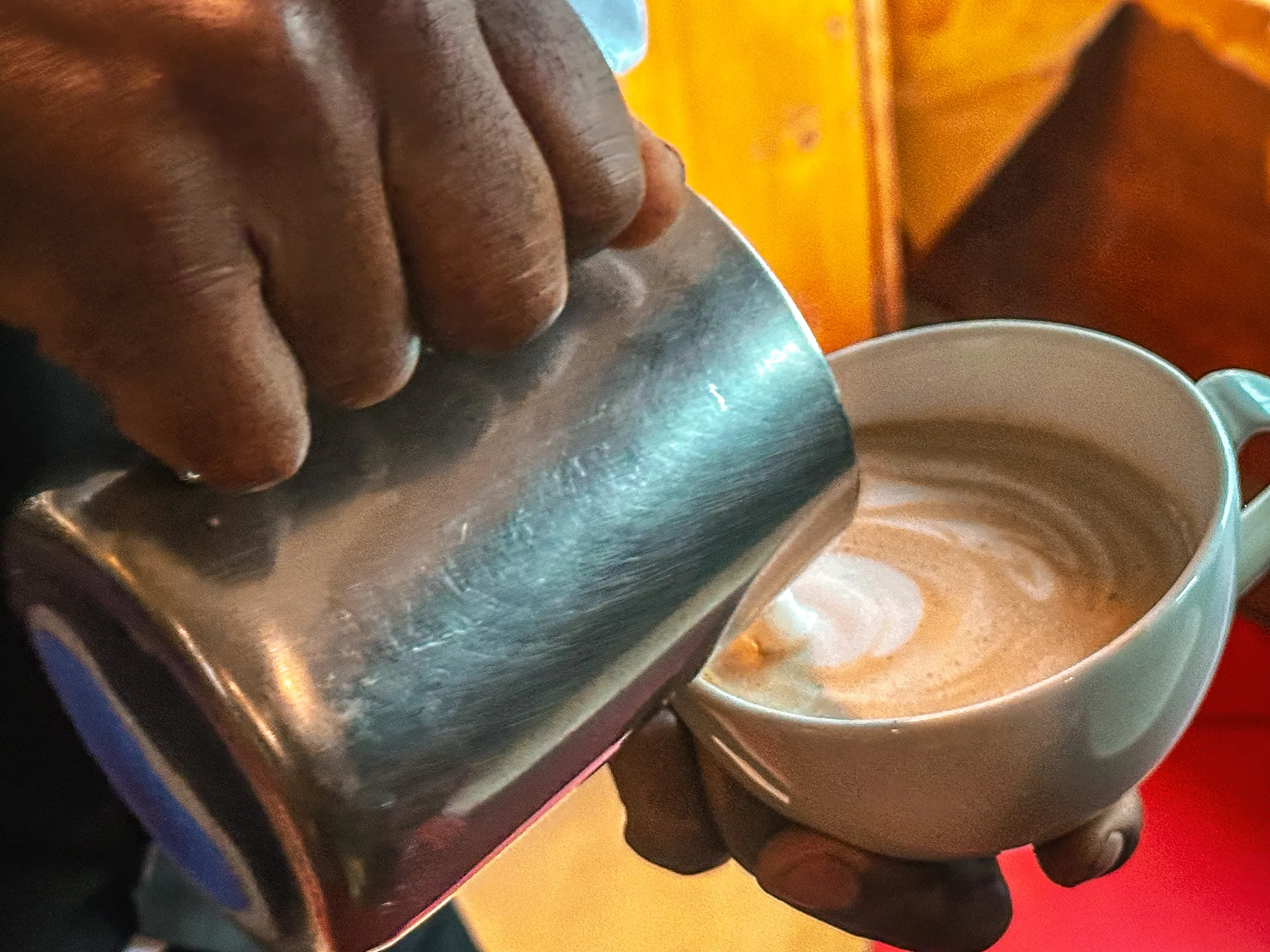 Steamed milk being poured from a jug into a cappuccino cup