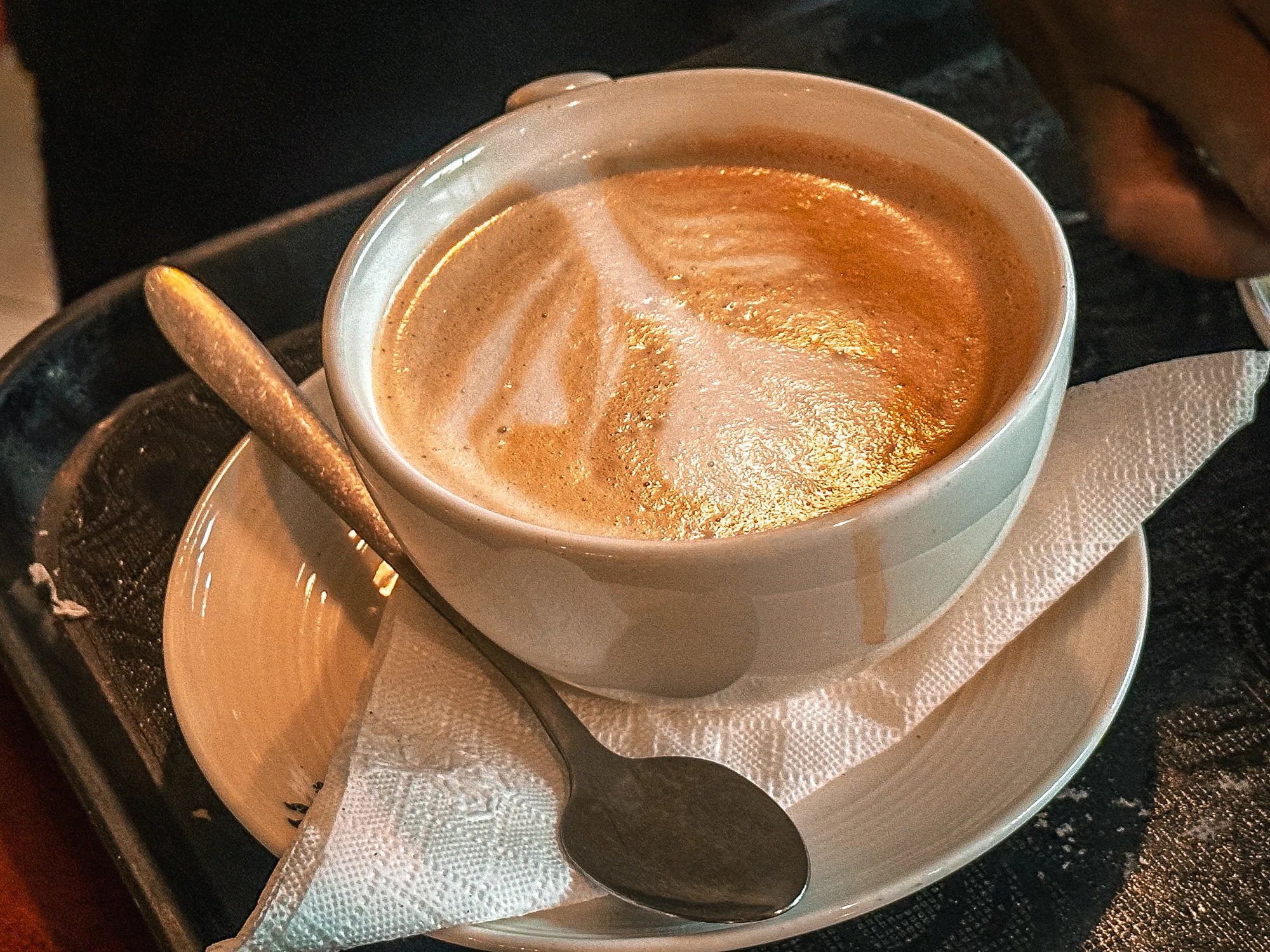 A cappuccino with leaf latte art in a white cup and saucer with a spoon