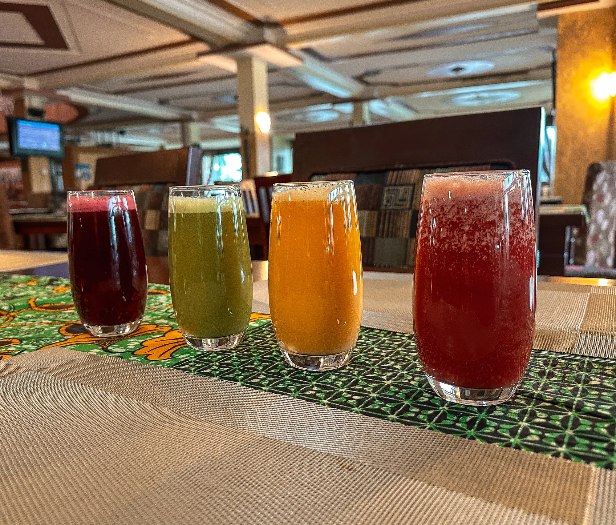 Four tall glasses of fresh juice in red, green and orange on a printed cloth in the restaurant