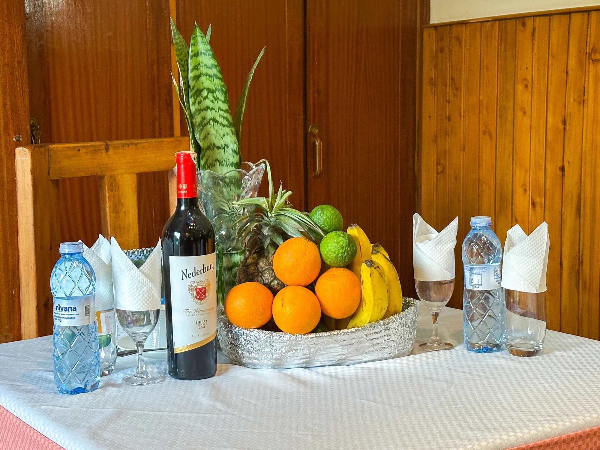 A welcome tray with a bottle of red wine, still water, glasses and a bowl of fresh fruit on a table
