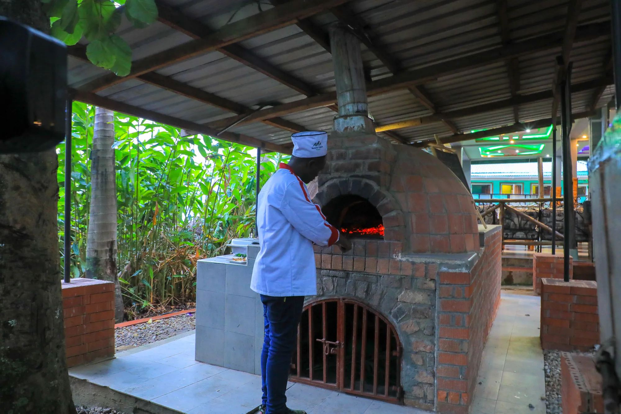 A chef in whites tending the brick pizza oven on the open-sided garden terrace