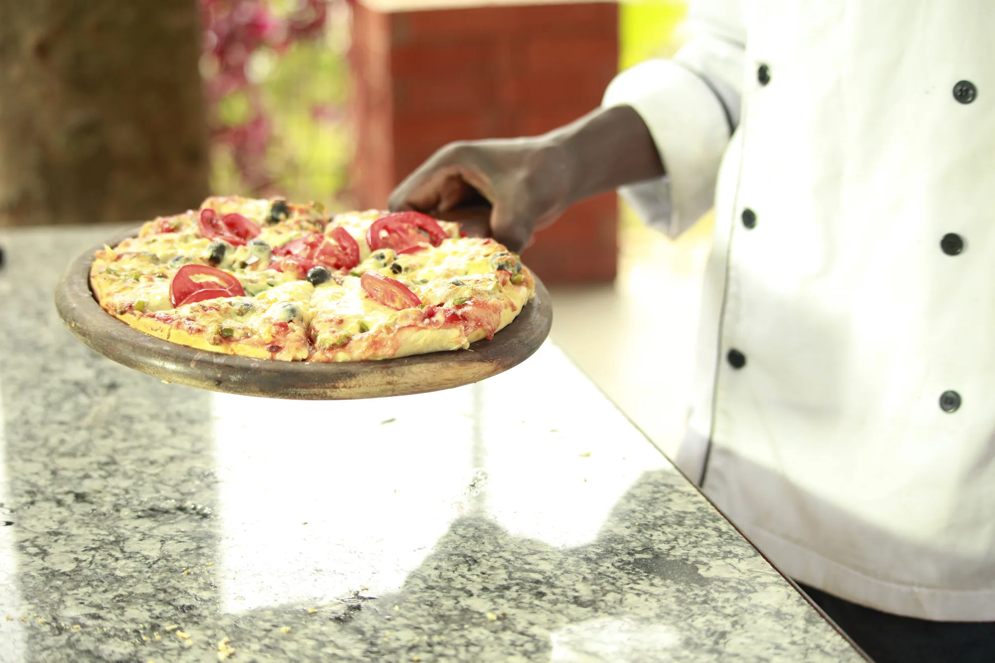 A cook's hands sliding a pizza on a round tray onto a stone counter