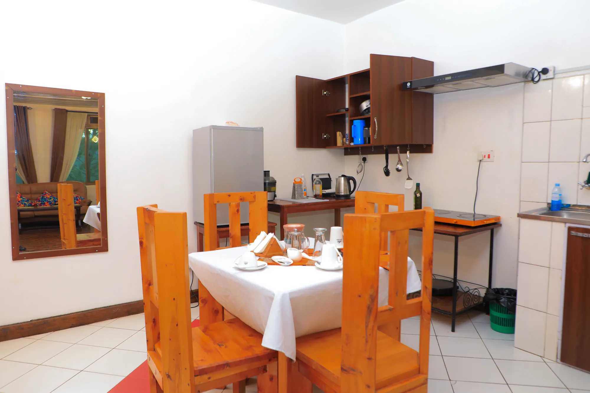A private dining table laid with a white cloth beside a small kitchenette with a fridge and cupboards