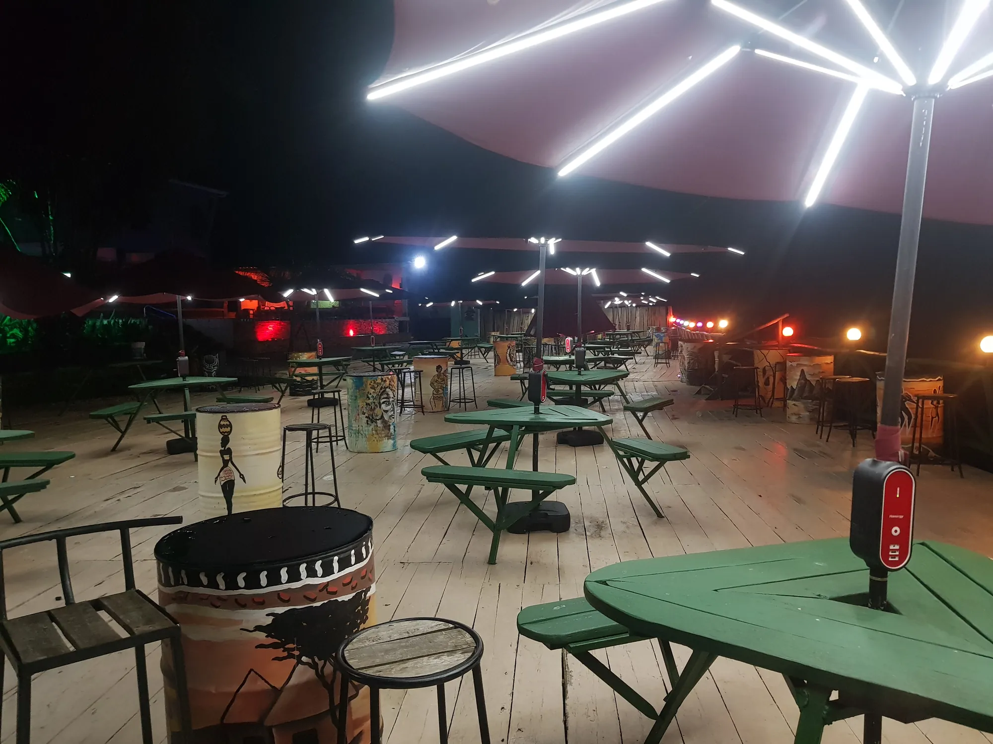 The deck at night with closed parasols, green picnic tables and a fire bowl