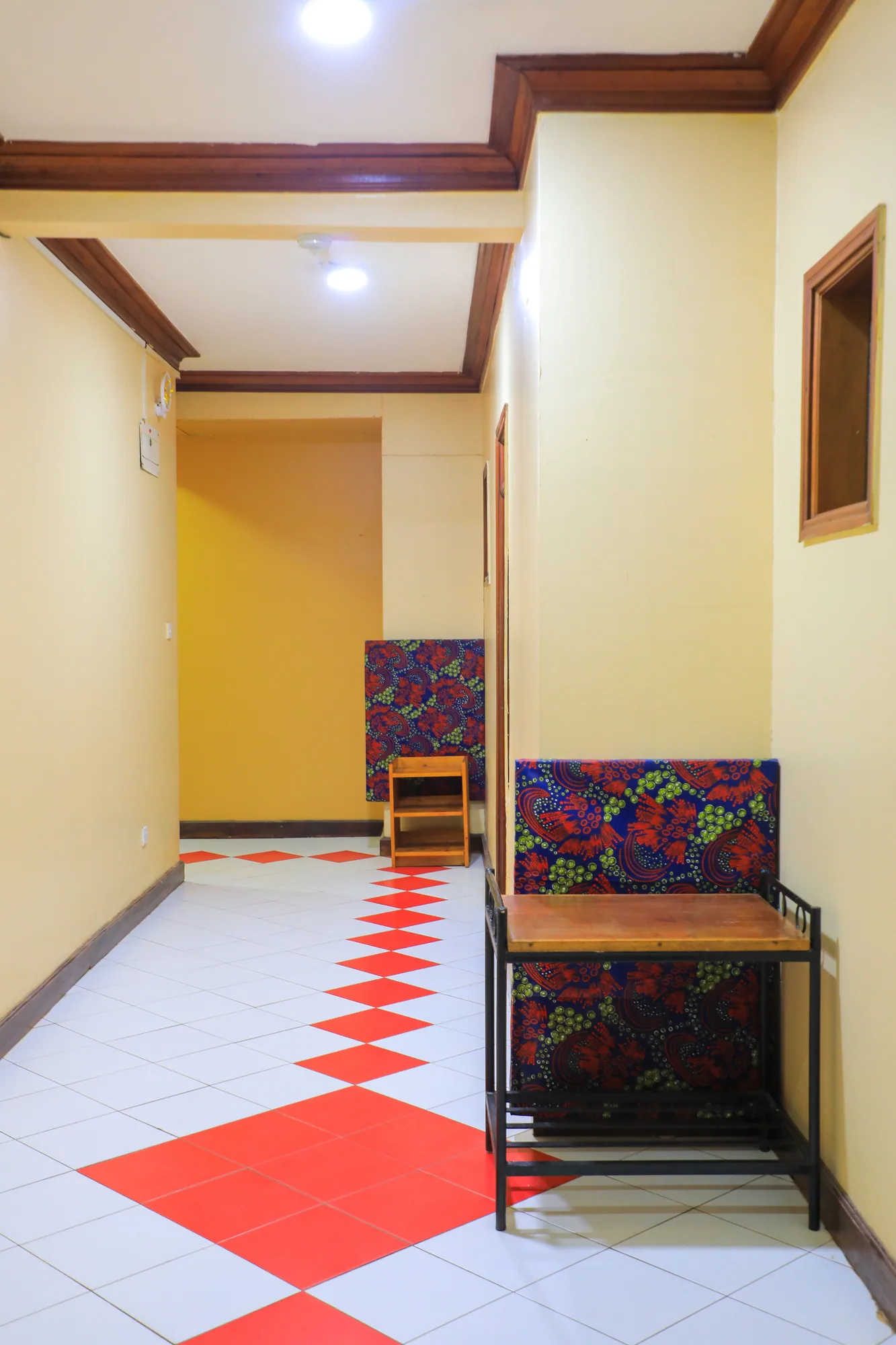 A room entrance corridor with a red and white tiled floor and a print-cushioned chair