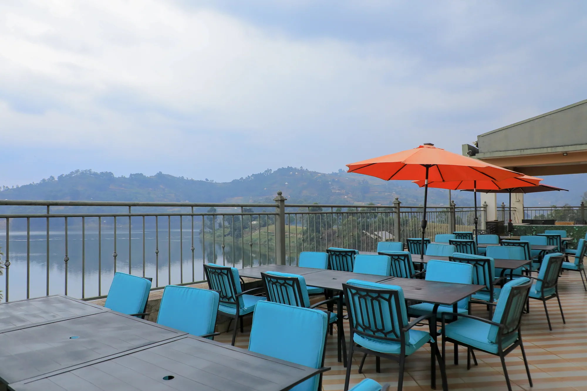 A rooftop terrace with turquoise-cushioned chairs, tables and a red parasol above the lake