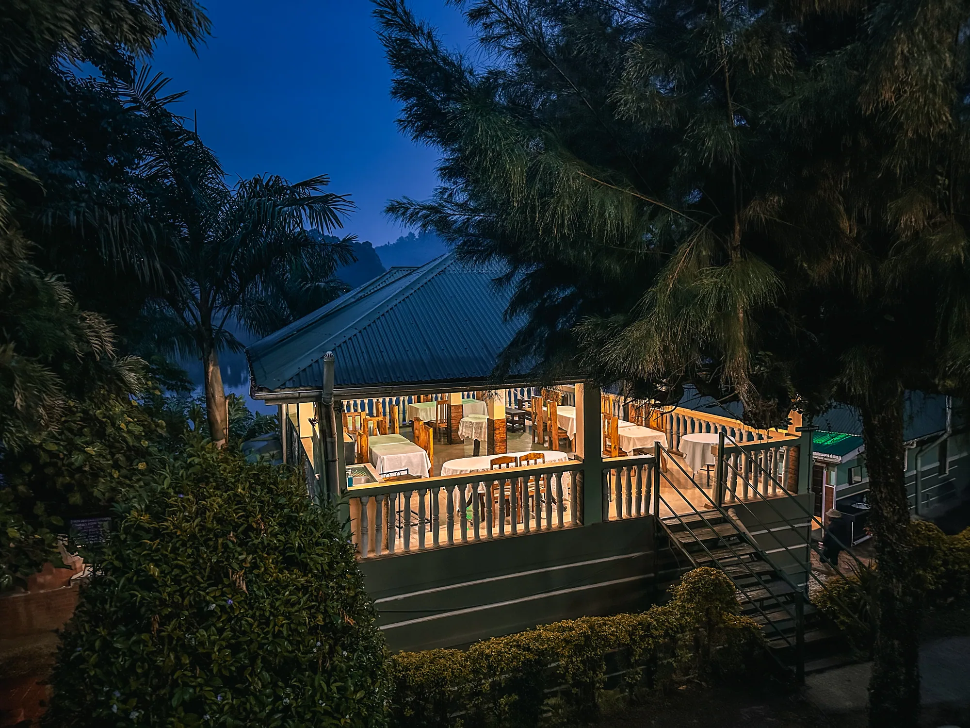 The timber-decked lodge veranda floodlit at dusk among tall trees