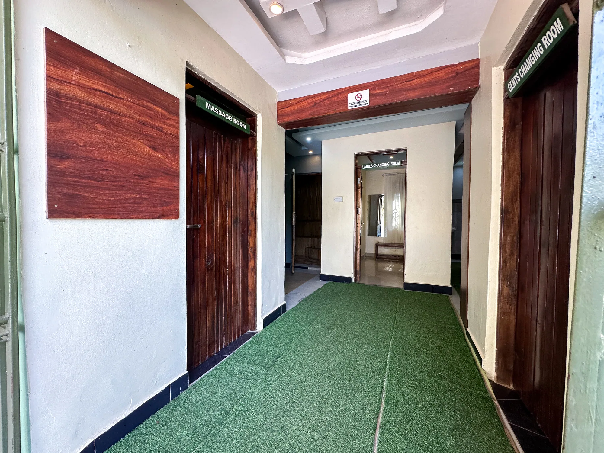 An interior corridor with green carpet, timber doors and signed rooms
