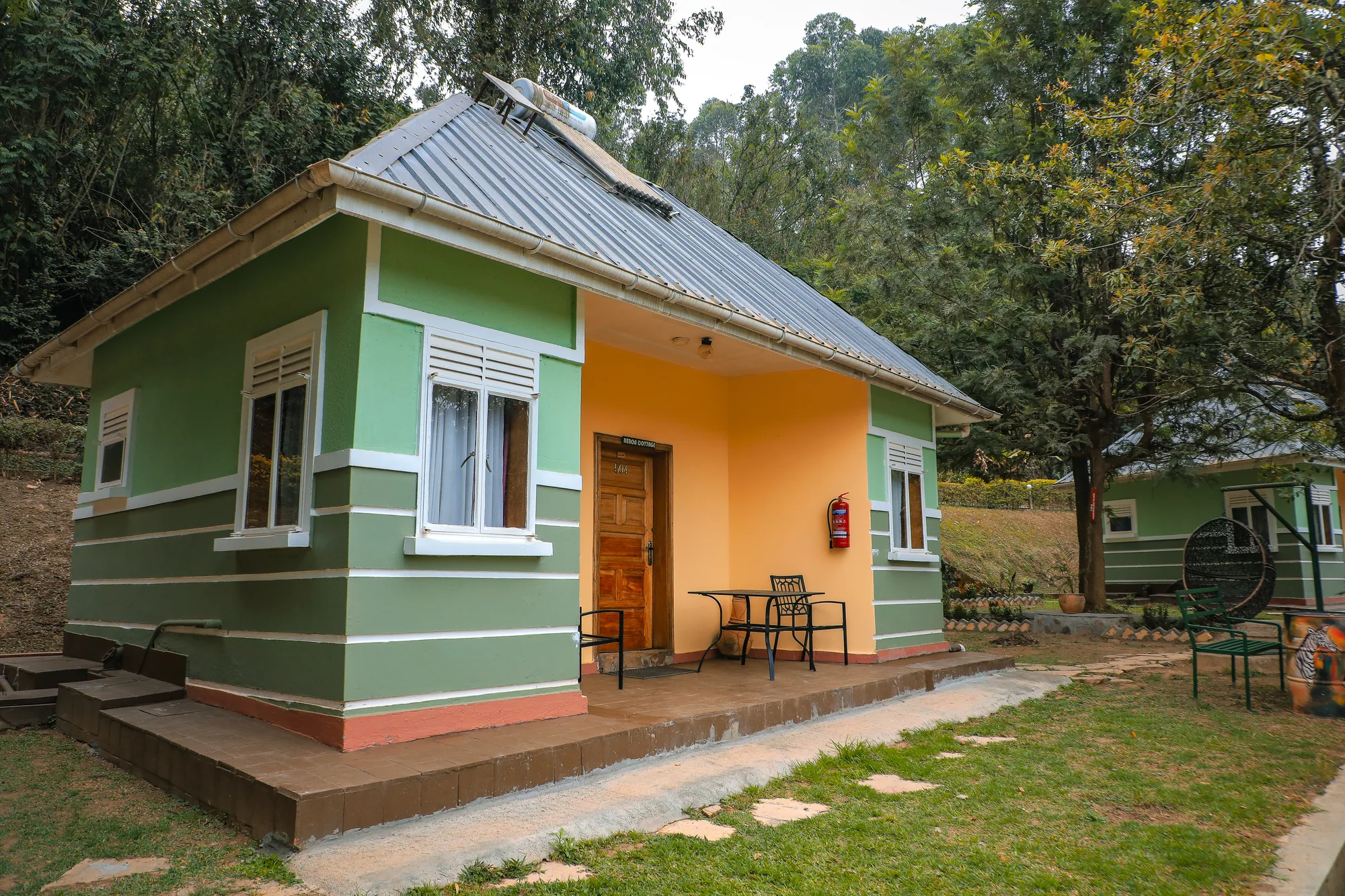 A green and cream cottage with its door open and a small table and chair outside