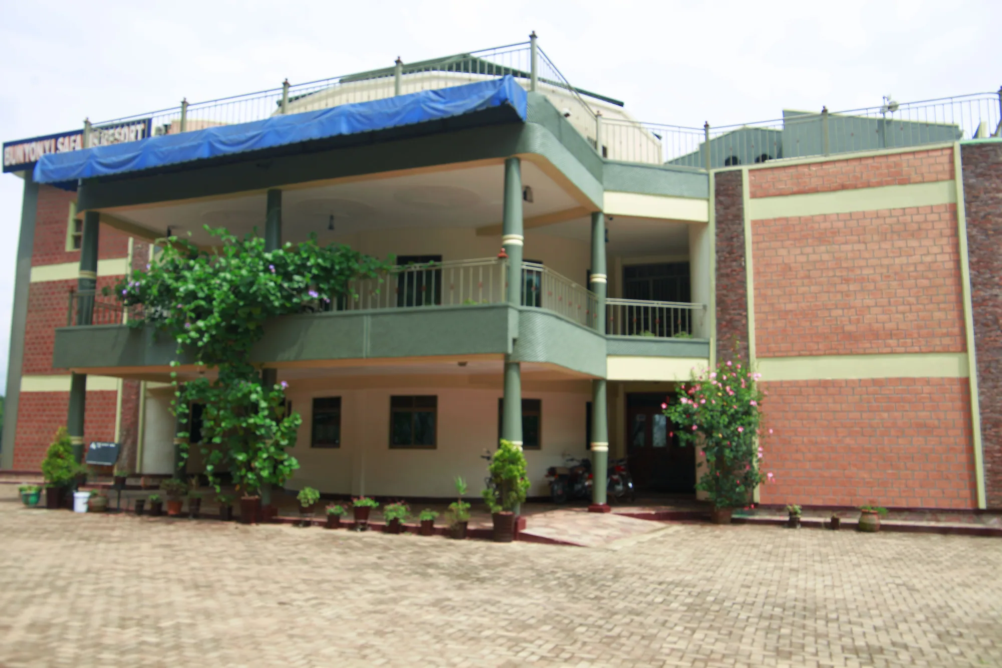 Front of the green and brick hotel building with its first-floor balcony and potted plants