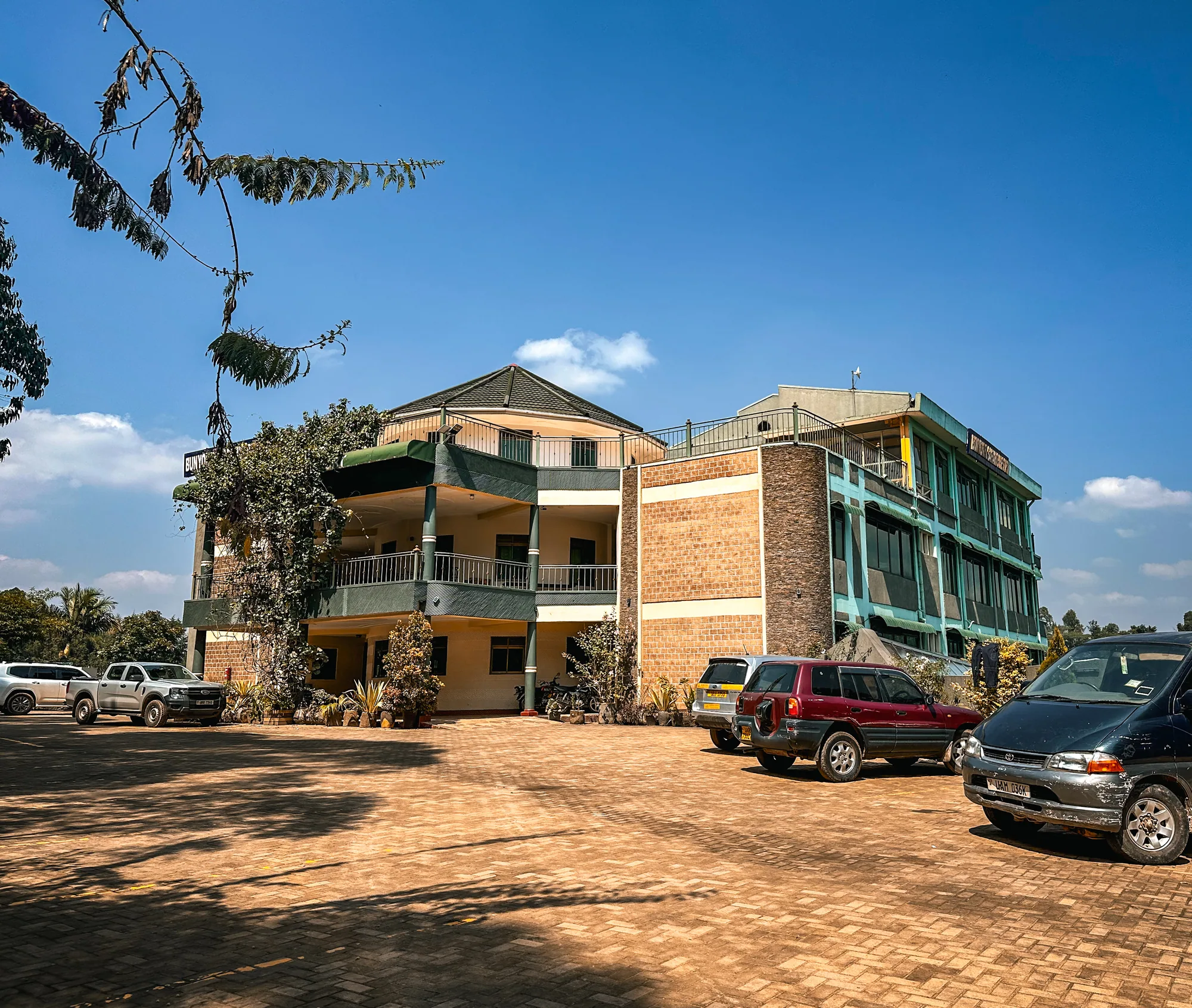 A three-storey brick and cream accommodation block with cars parked on the earth forecourt