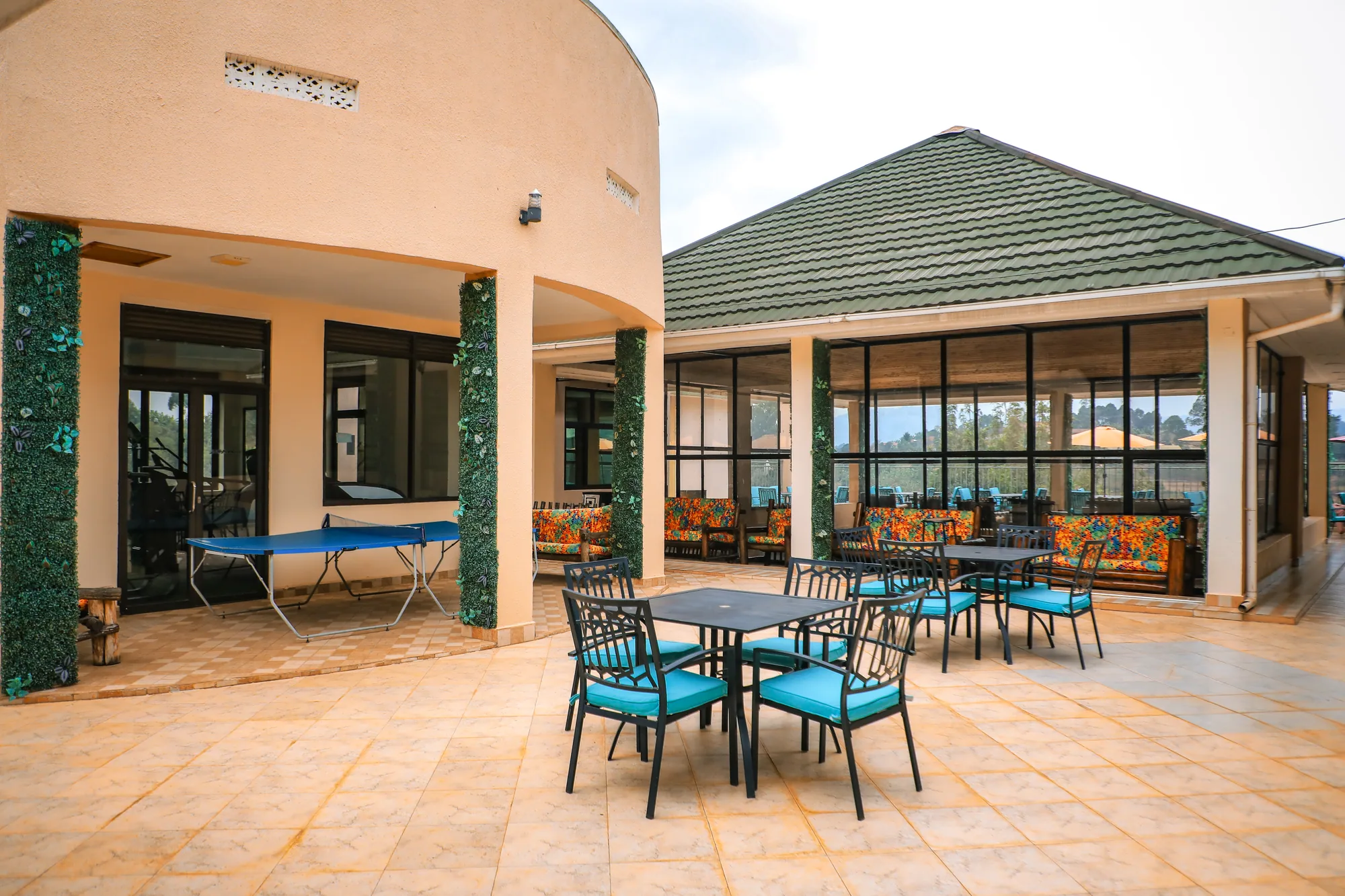 A covered veranda with turquoise-cushioned chairs and tables outside a green-roofed pavilion