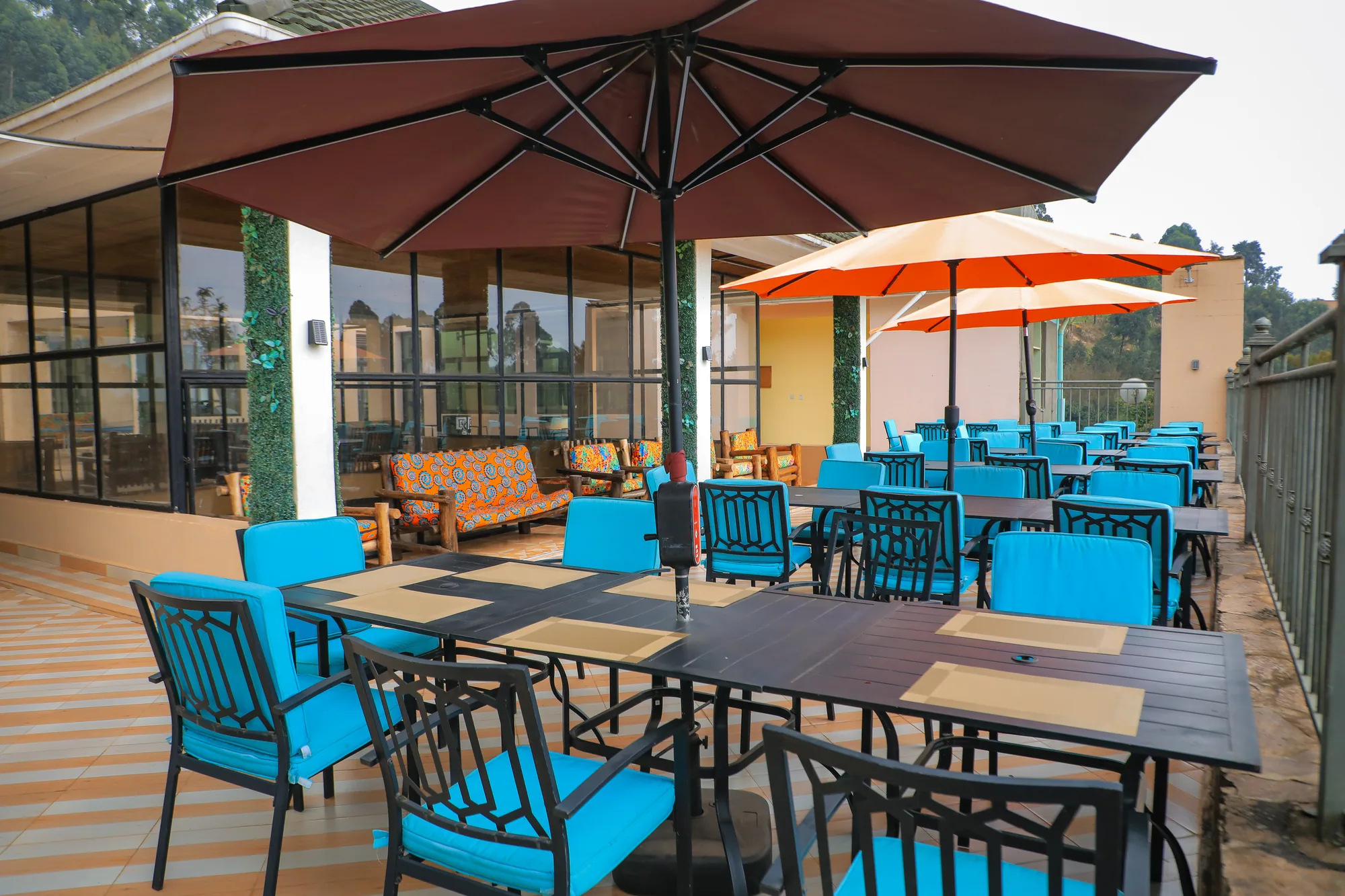 Decked terrace dining tables under maroon and orange parasols beside the building