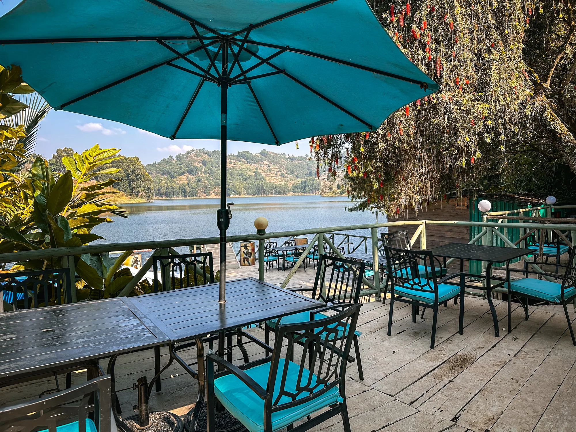 Terrace tables under a turquoise parasol on the timber deck at the water's edge