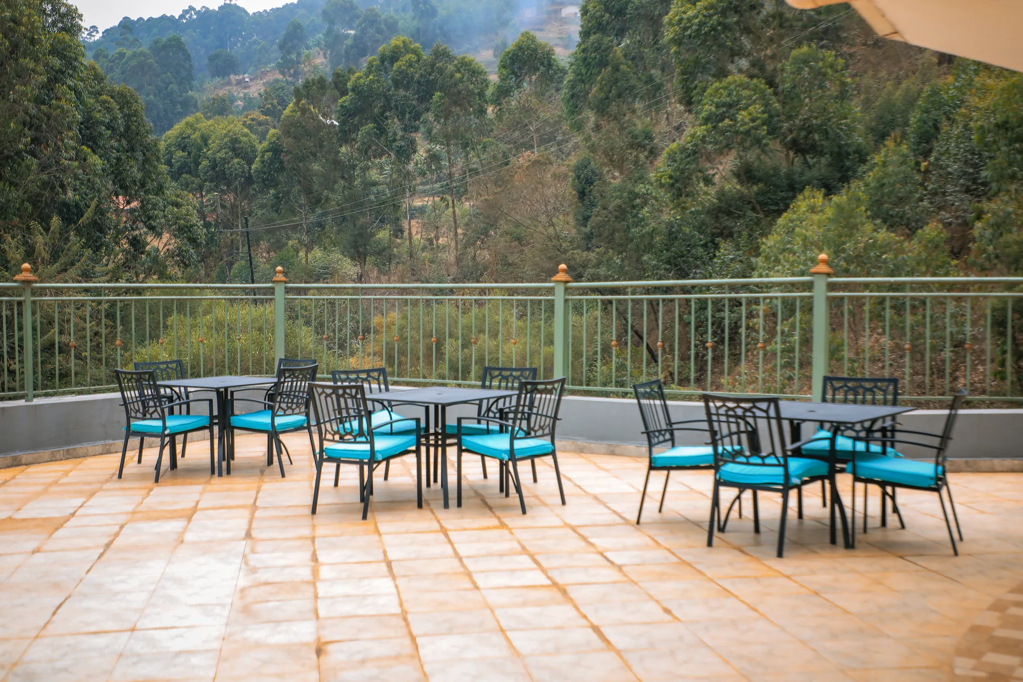 A tiled terrace with two sets of turquoise-cushioned chairs looking out to wooded hills
