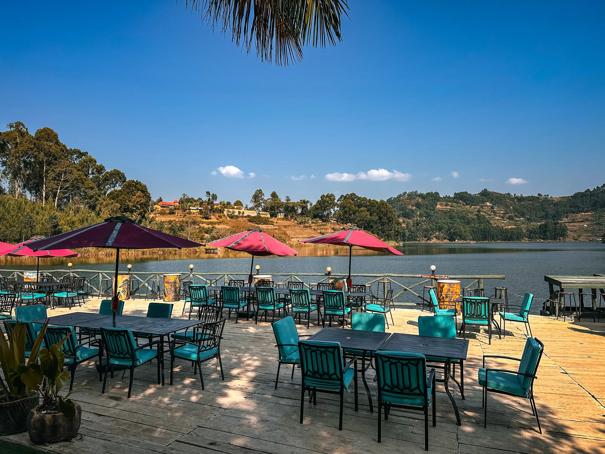 Terrace tables under pink parasols on the lawn beside the lake under a clear sky