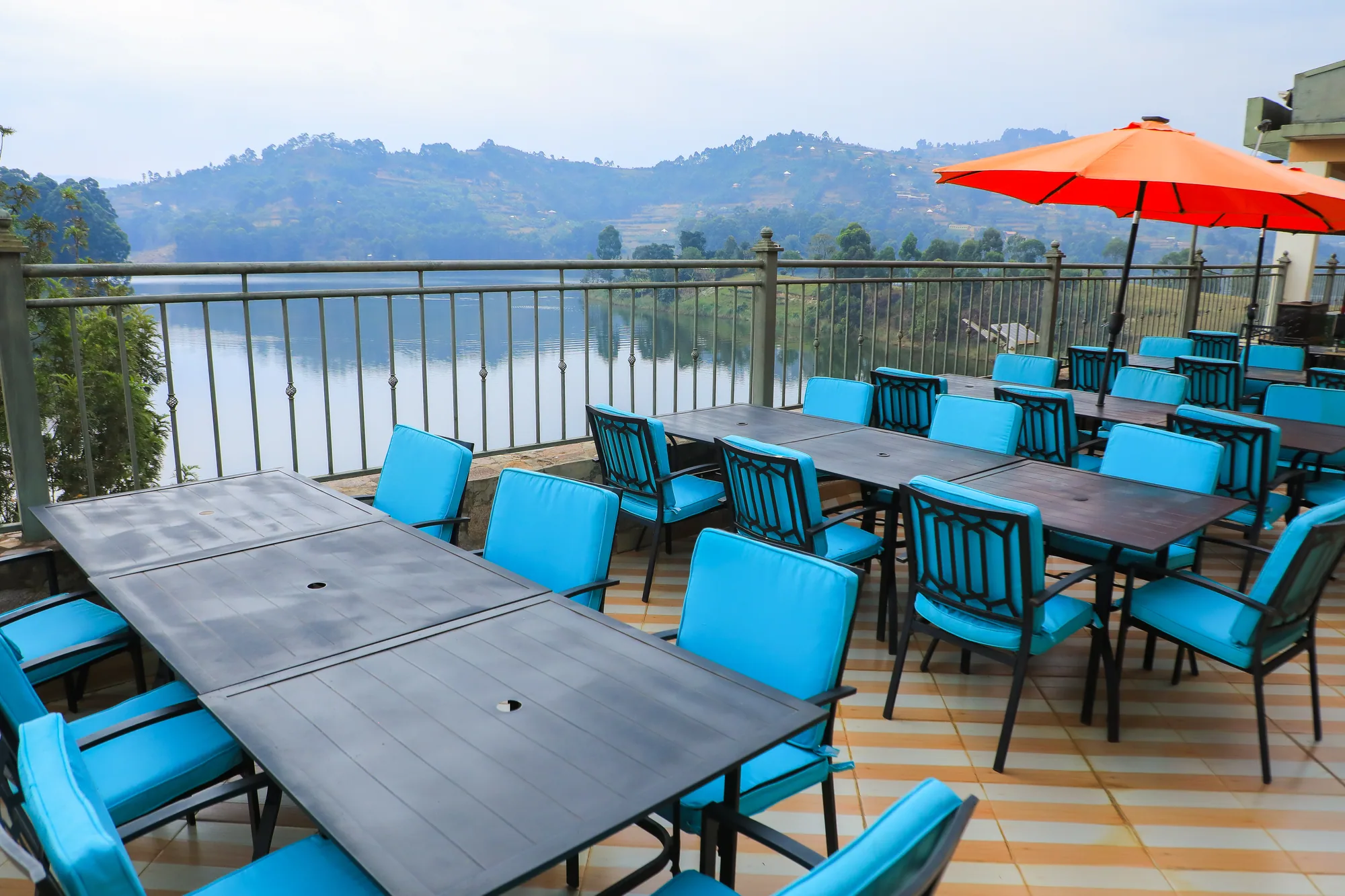A long dining table on the deck with a red parasol, looking down the lake to the hills
