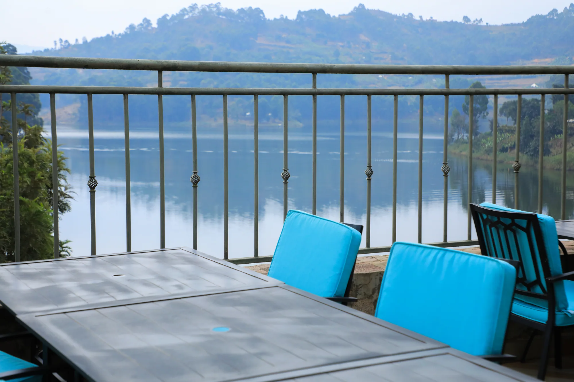 A terrace table with turquoise cushions against the railing, the calm lake beyond