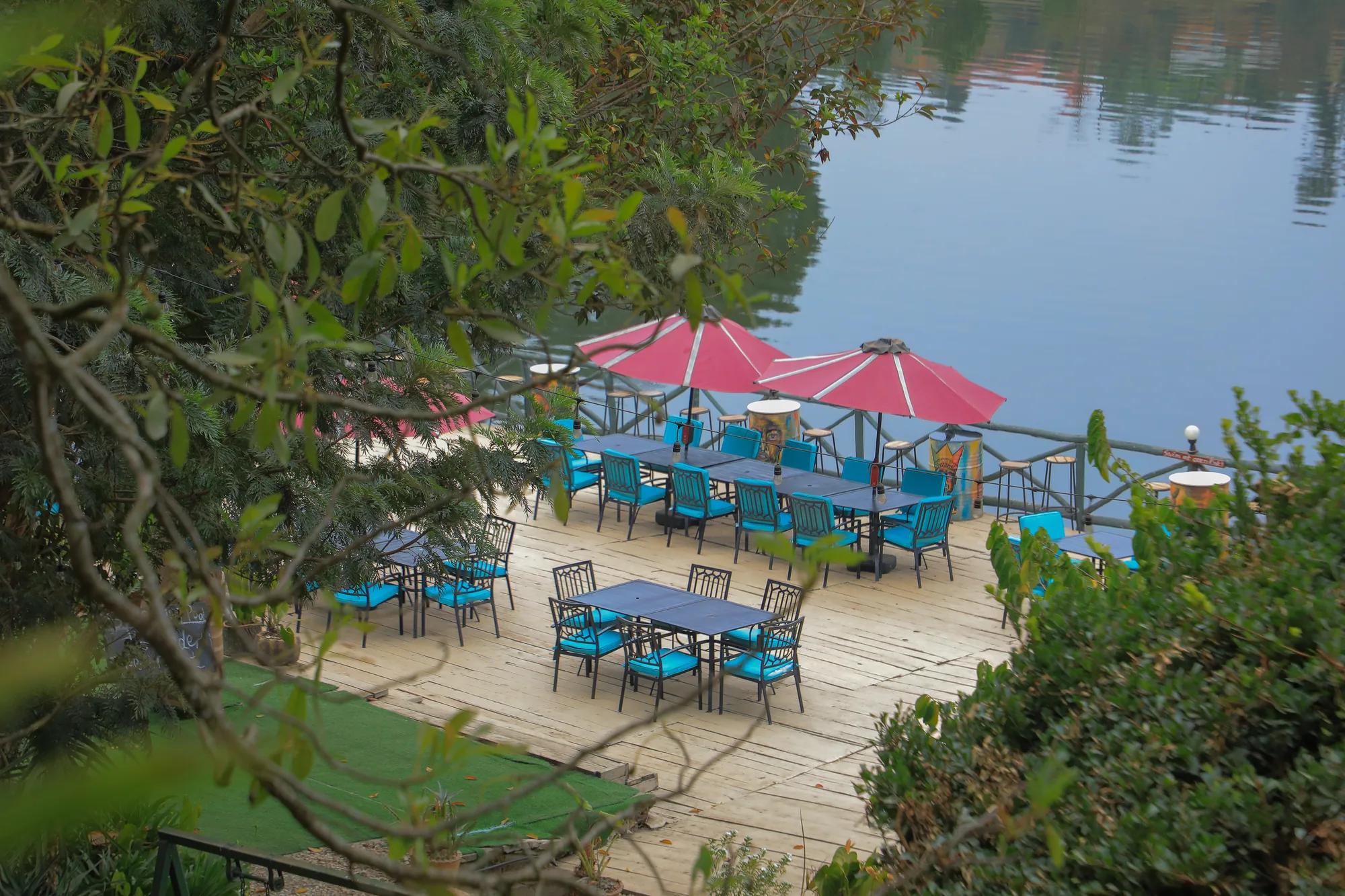 Lakeside deck tables under pink parasols seen from the garden above
