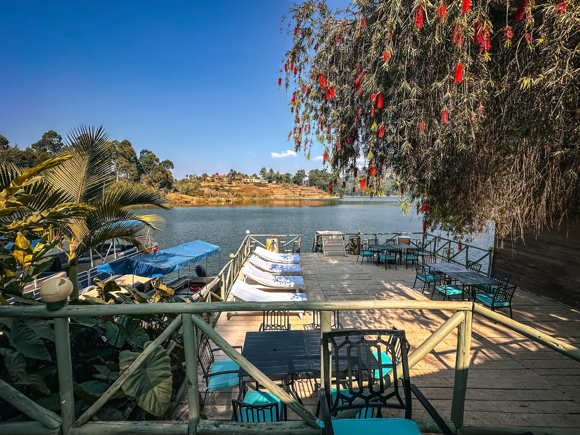 The jetty deck with moored boats beside terrace furniture and flowering shrubs