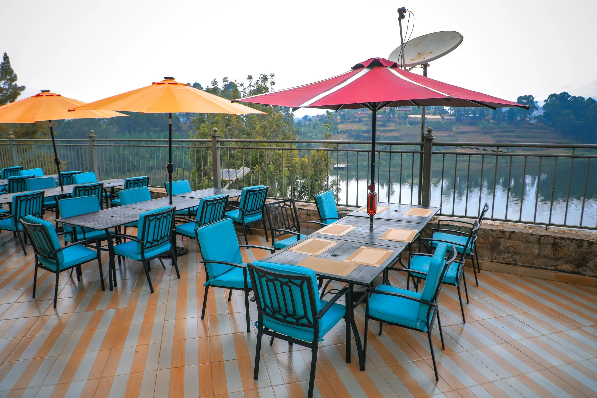 Terrace tables under orange and red parasols with a satellite dish on the roof behind