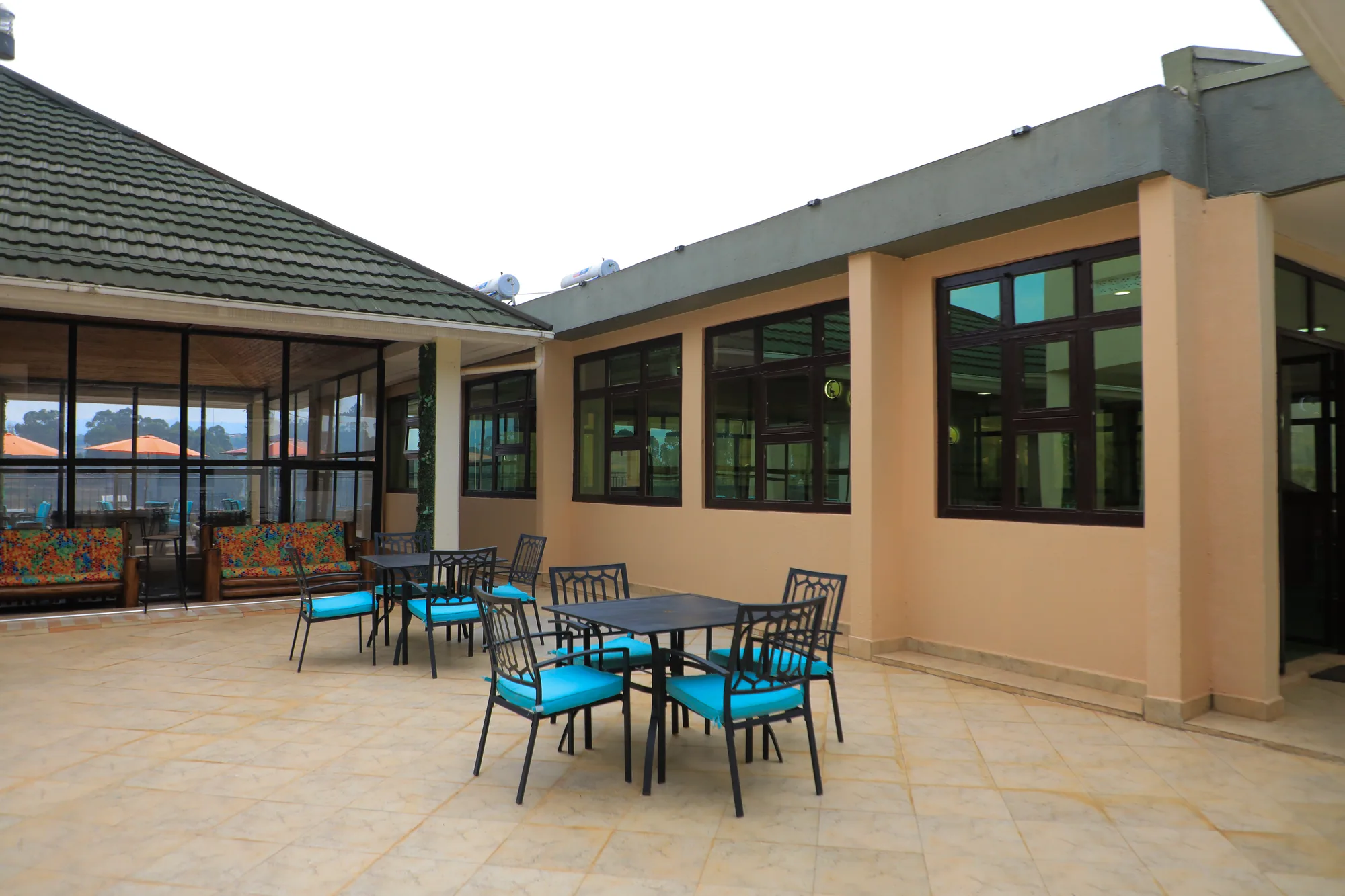 A paved veranda with a single table and turquoise chairs outside tall windows
