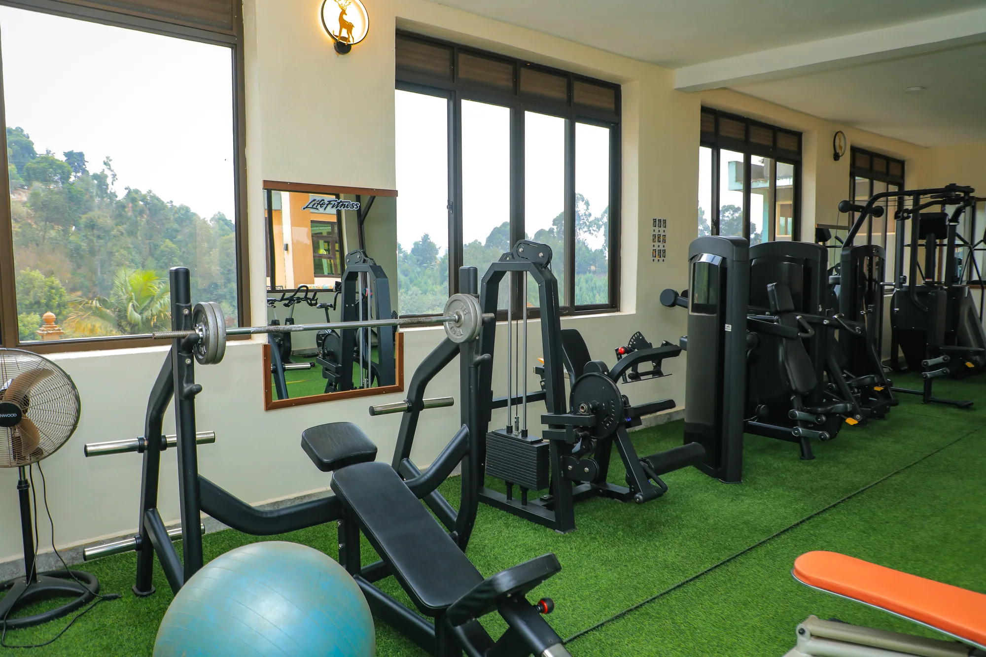 The gym with weight machines, a bench and an exercise ball on green flooring beside a mirrored wall