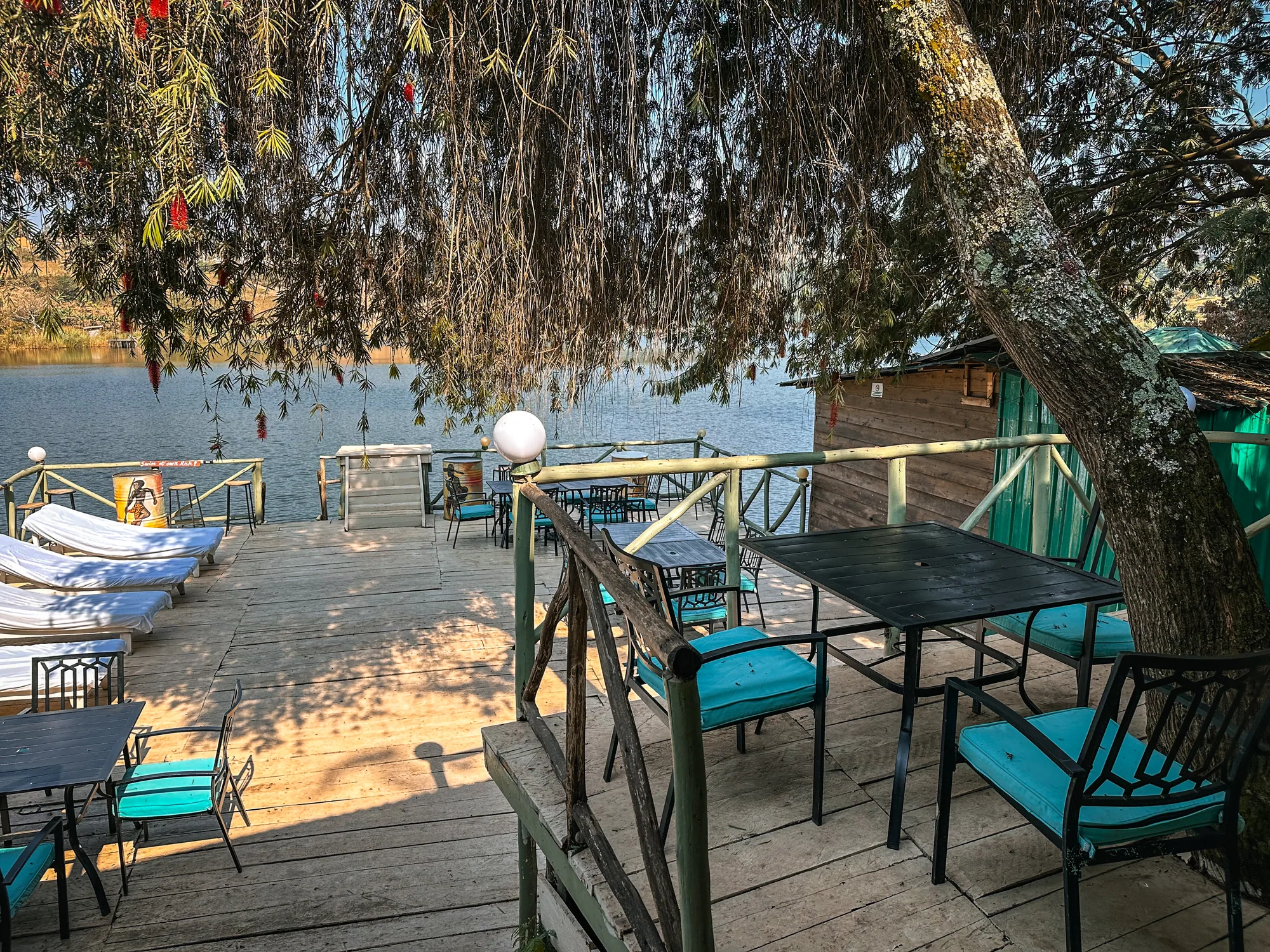 Deck tables and sun loungers under an overhanging tree at the water's edge
