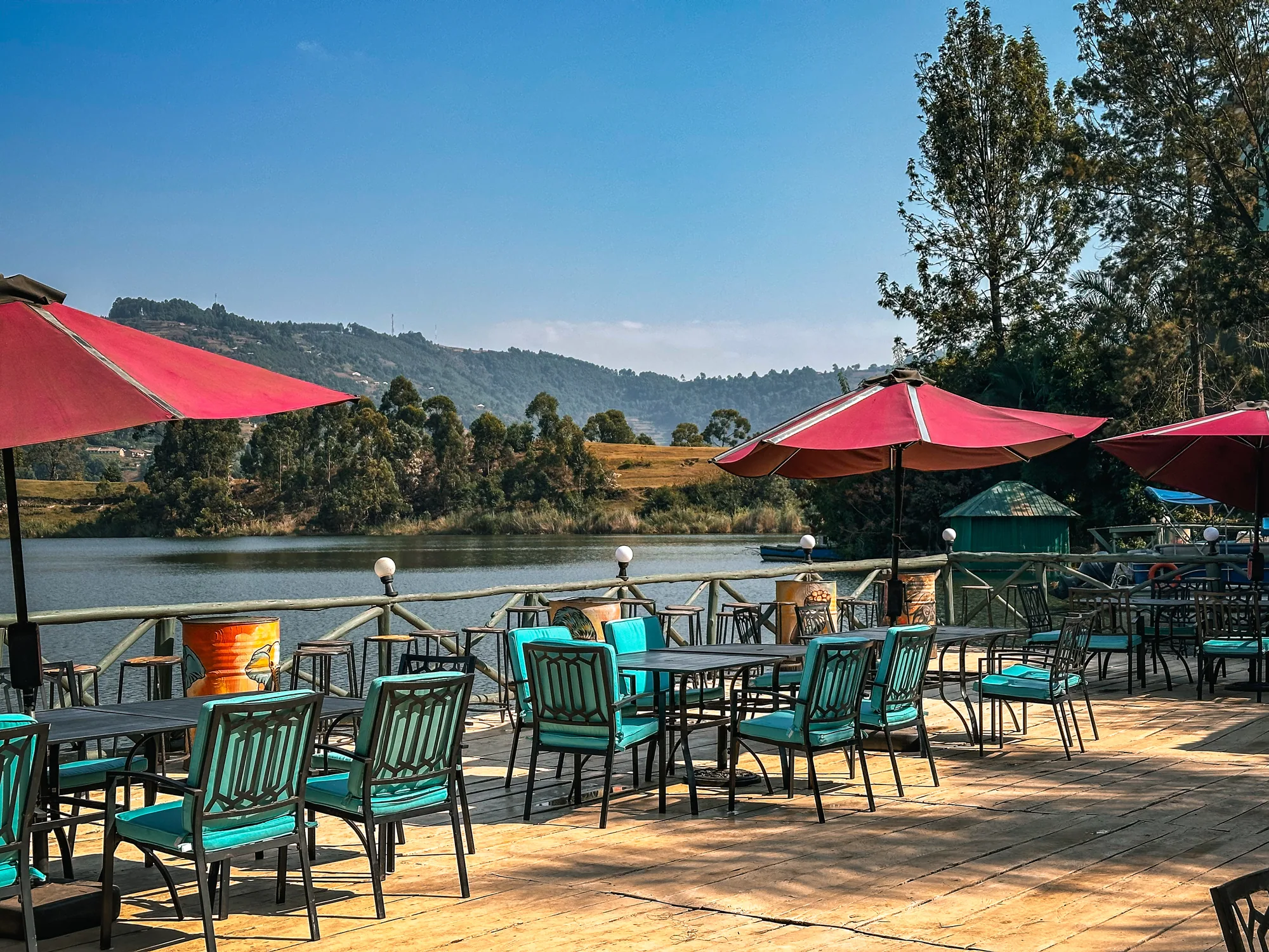 A broad deck with red parasols and turquoise chairs looking across the lake to farmed slopes