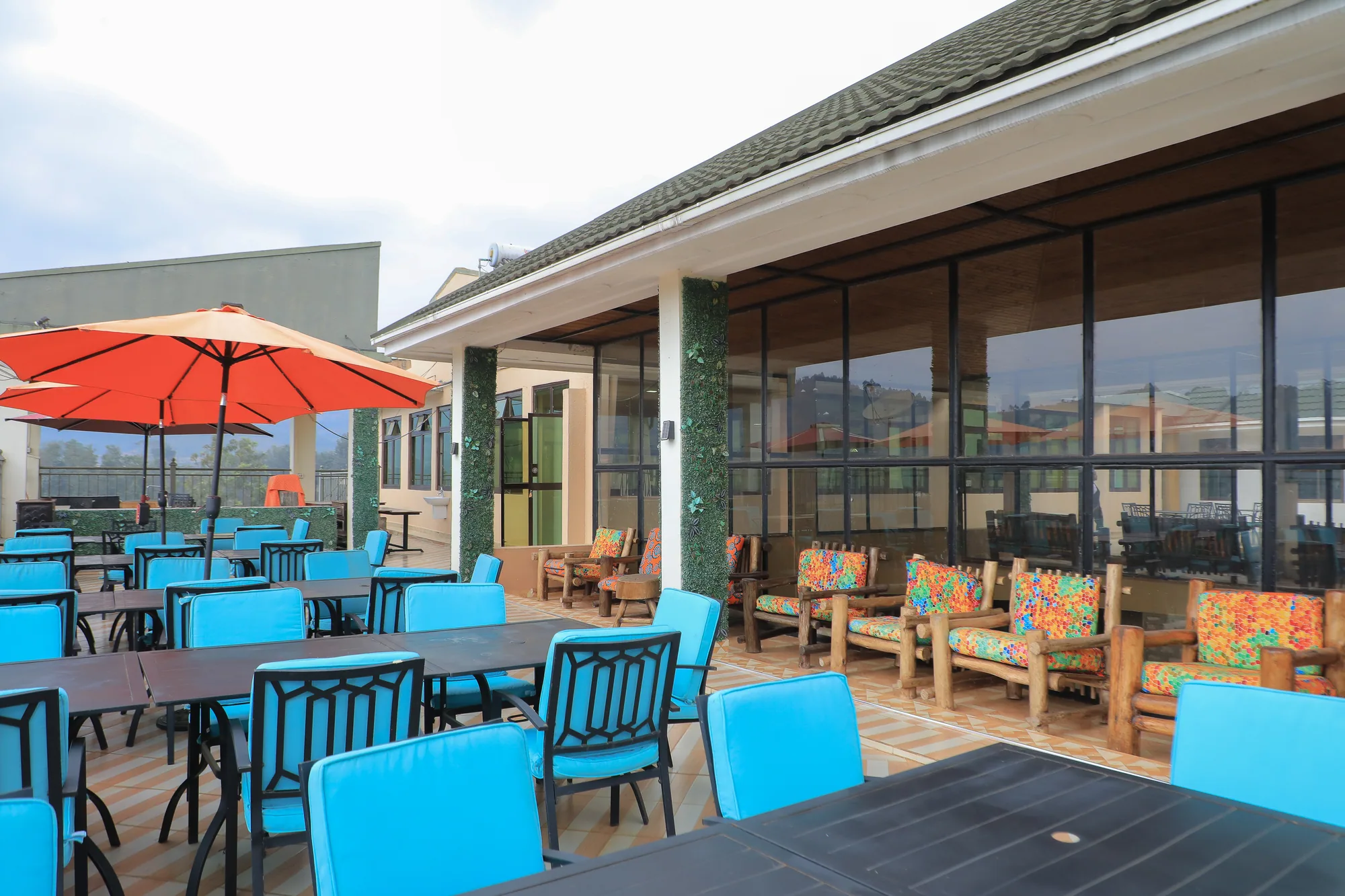 A terrace with a red parasol, turquoise chairs and printed-cushion benches against the glass frontage