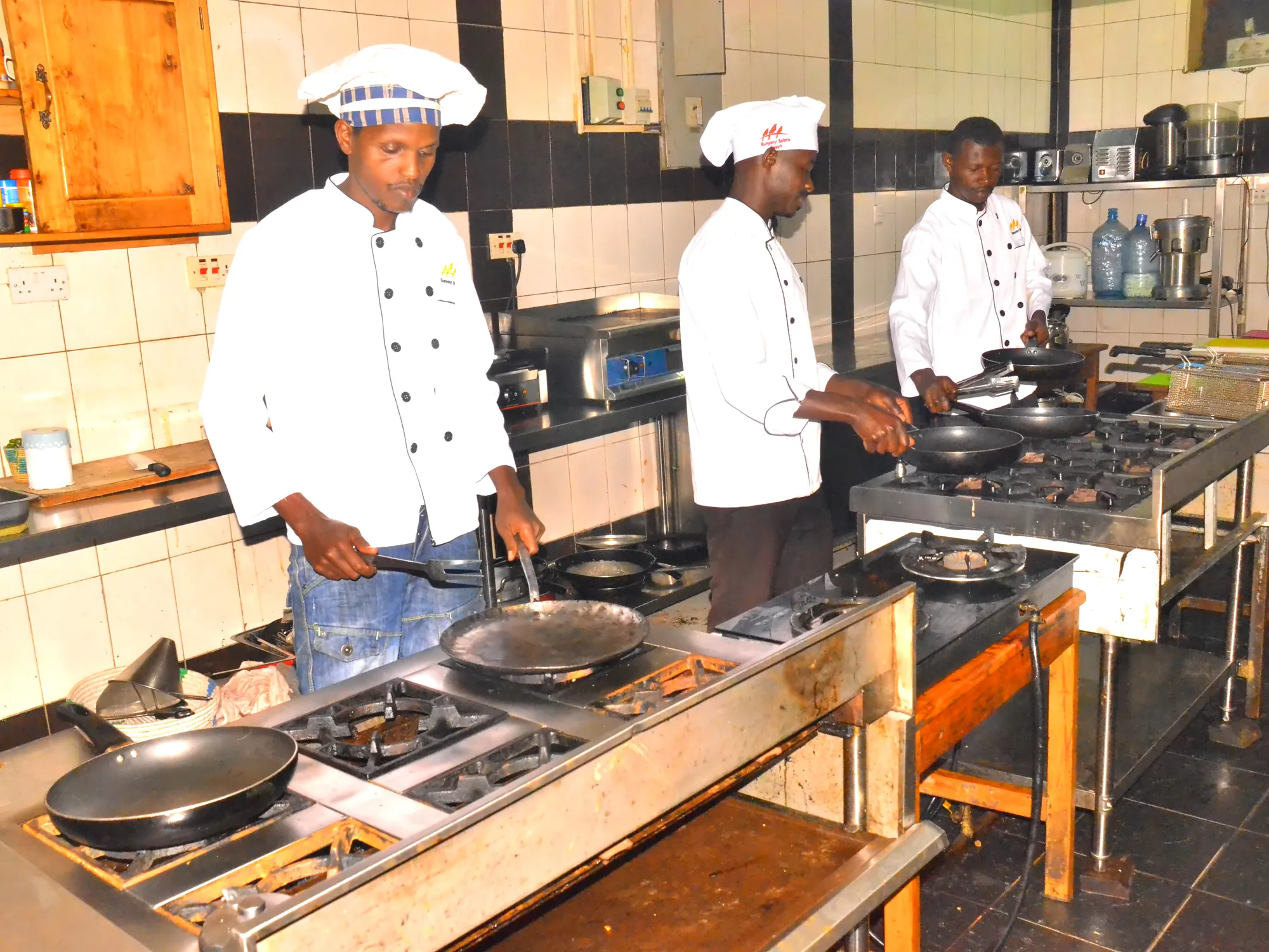 Three trainee cooks in chef's whites working at the gas ranges in the institute training kitchen