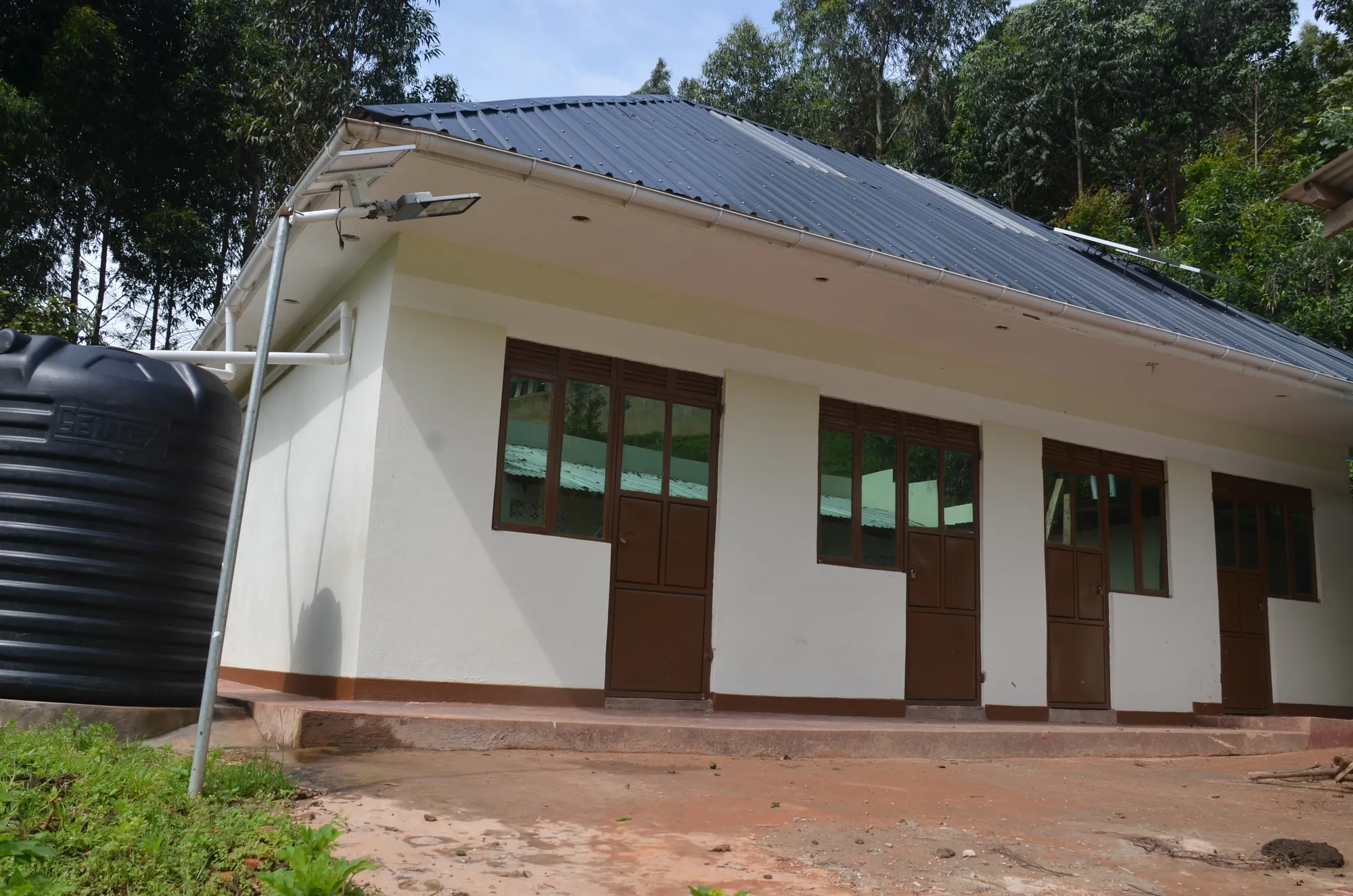 A white classroom block with a water tank at the gable end, still under finishing works