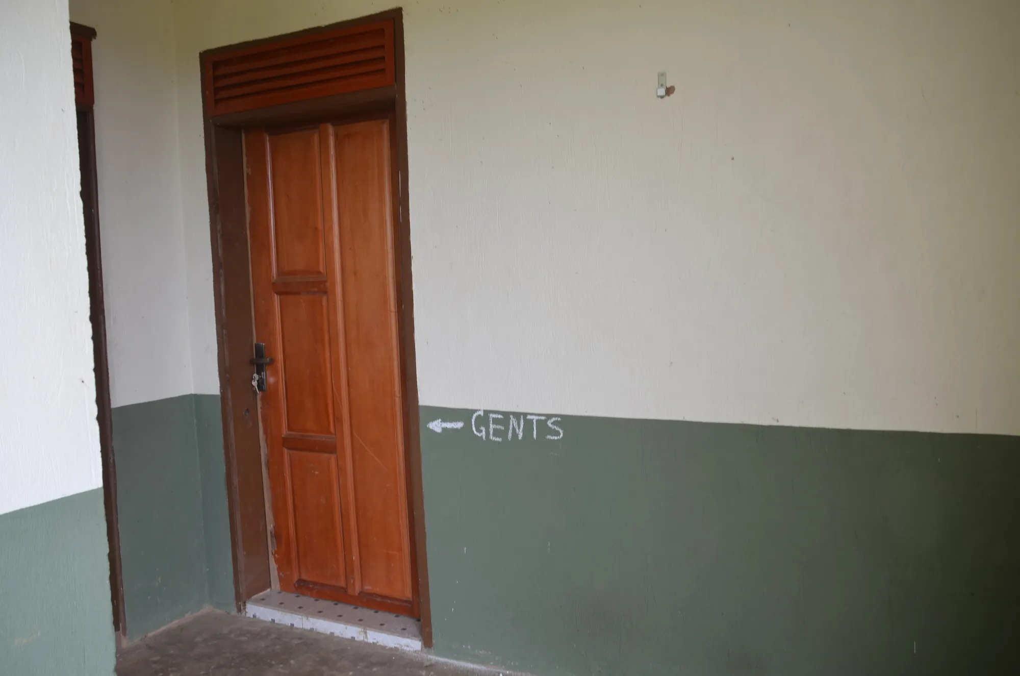 An interior wall with a timber door and a painted GENTS sign with an arrow