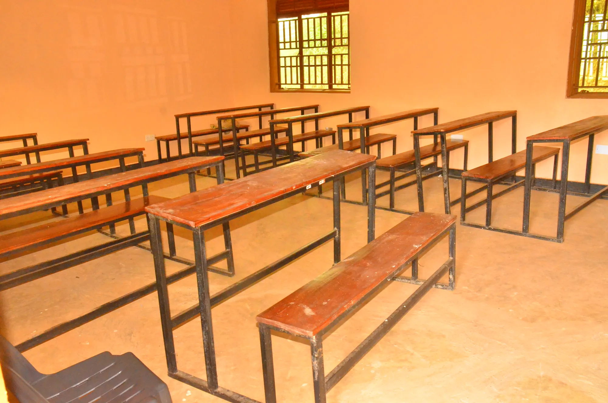 An empty classroom with steel-framed benches and desks and orange walls