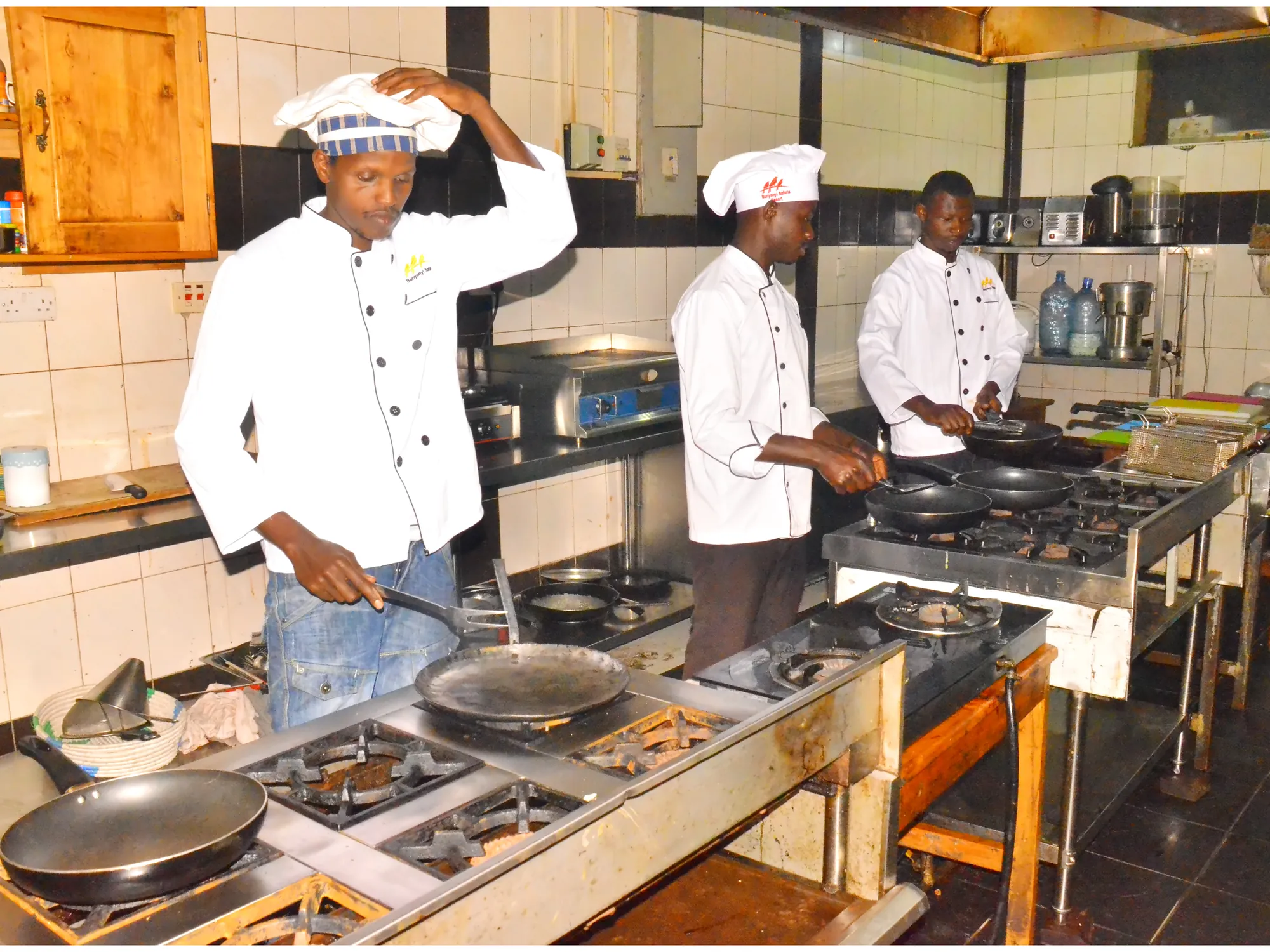 Trainee cooks in whites at the institute kitchen range with pans on the hobs