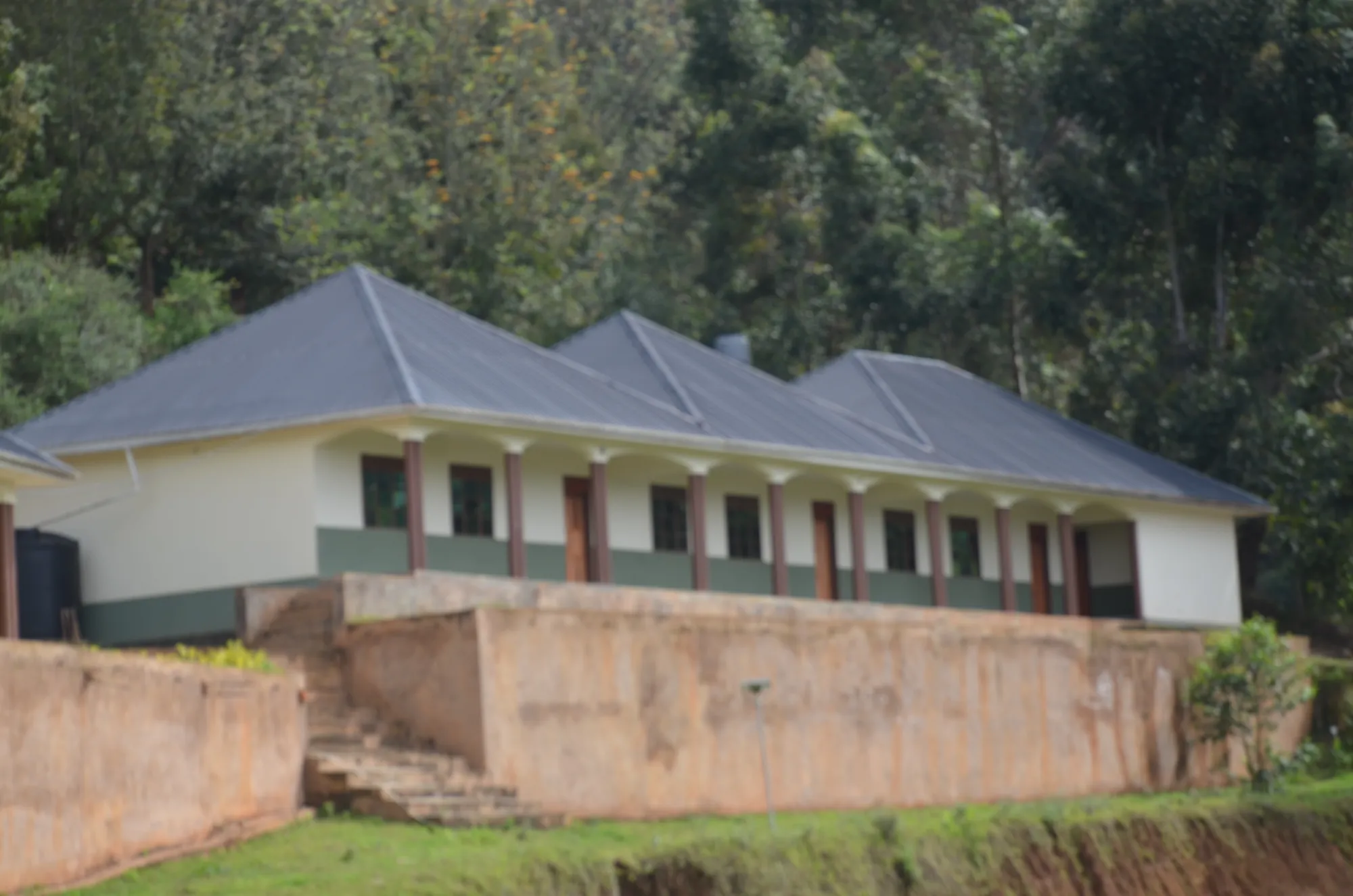 A long classroom block with a grey roof above a red earth retaining wall