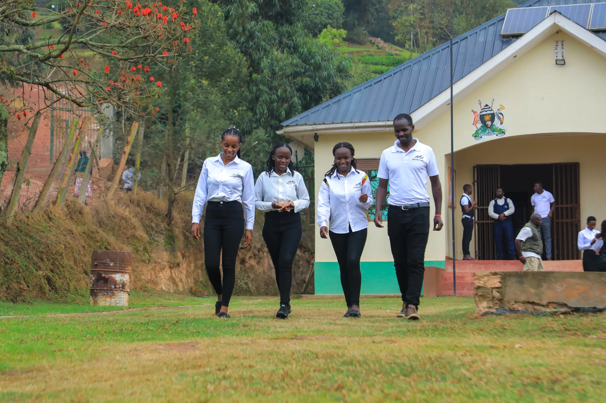 Four students in white shirts and dark trousers walking across the lawn from the institute entrance