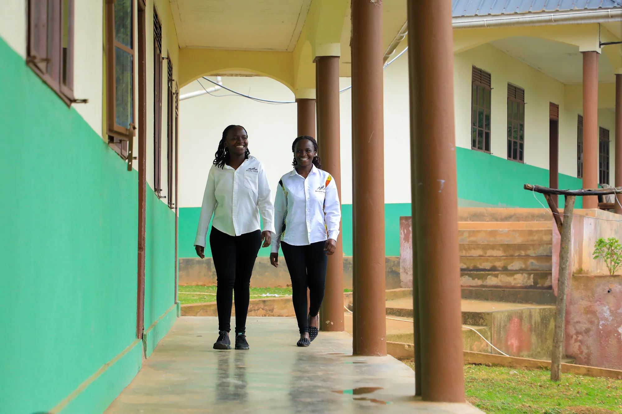 Two students walking along the covered veranda between the green-painted columns