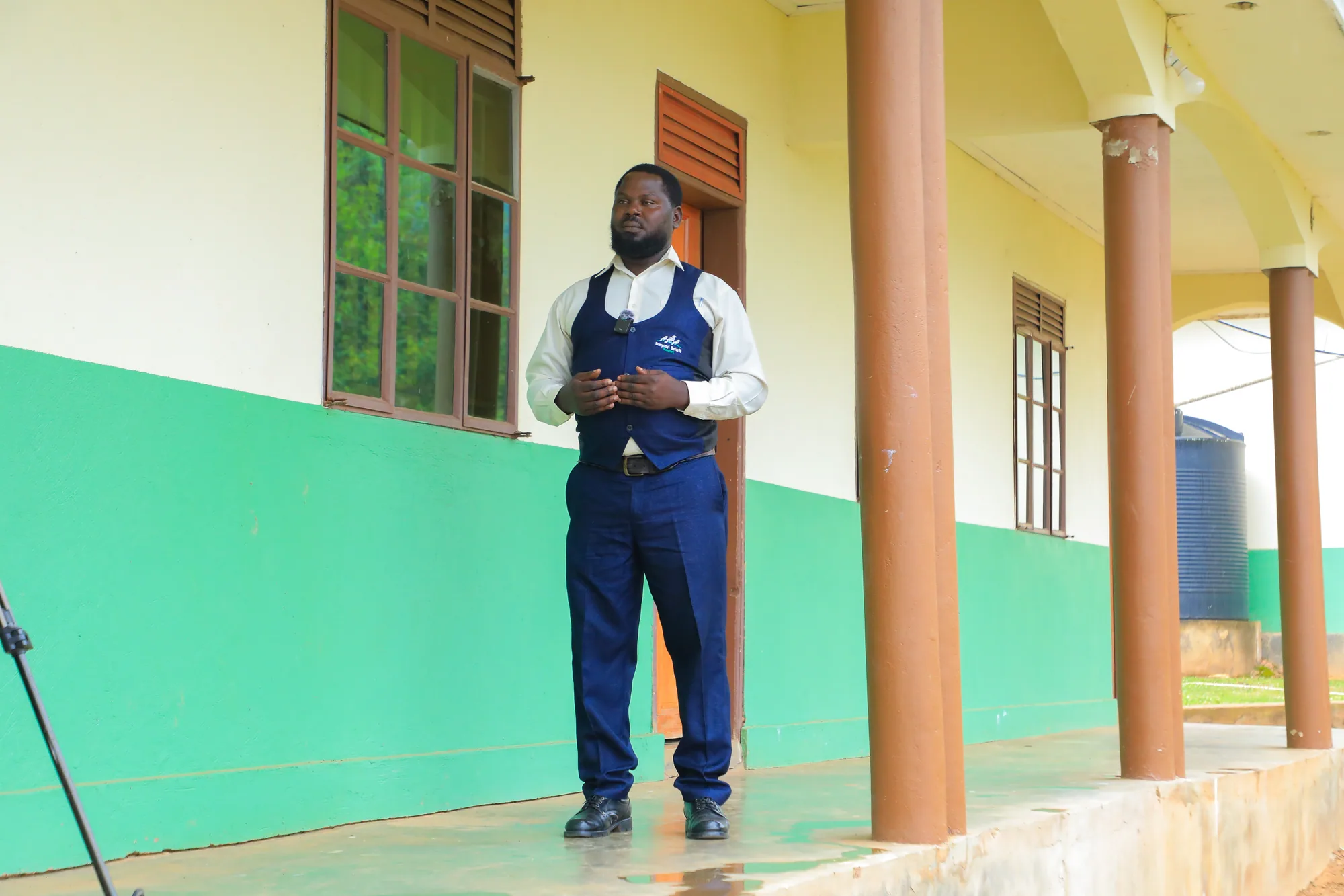 A student in a dark waistcoat standing on the veranda of a classroom block