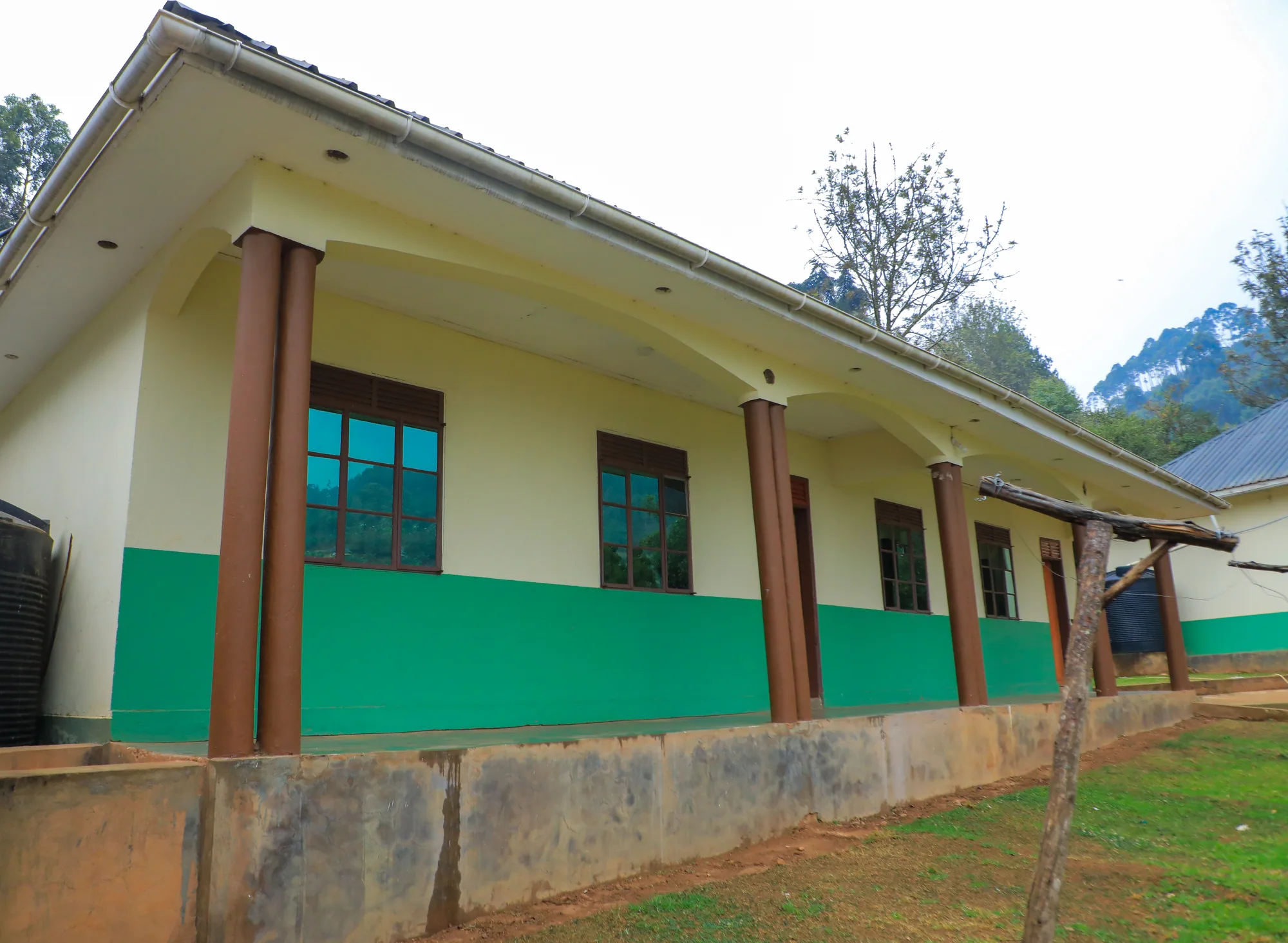 A green-banded classroom block with its veranda columns and a bare earth bank in front