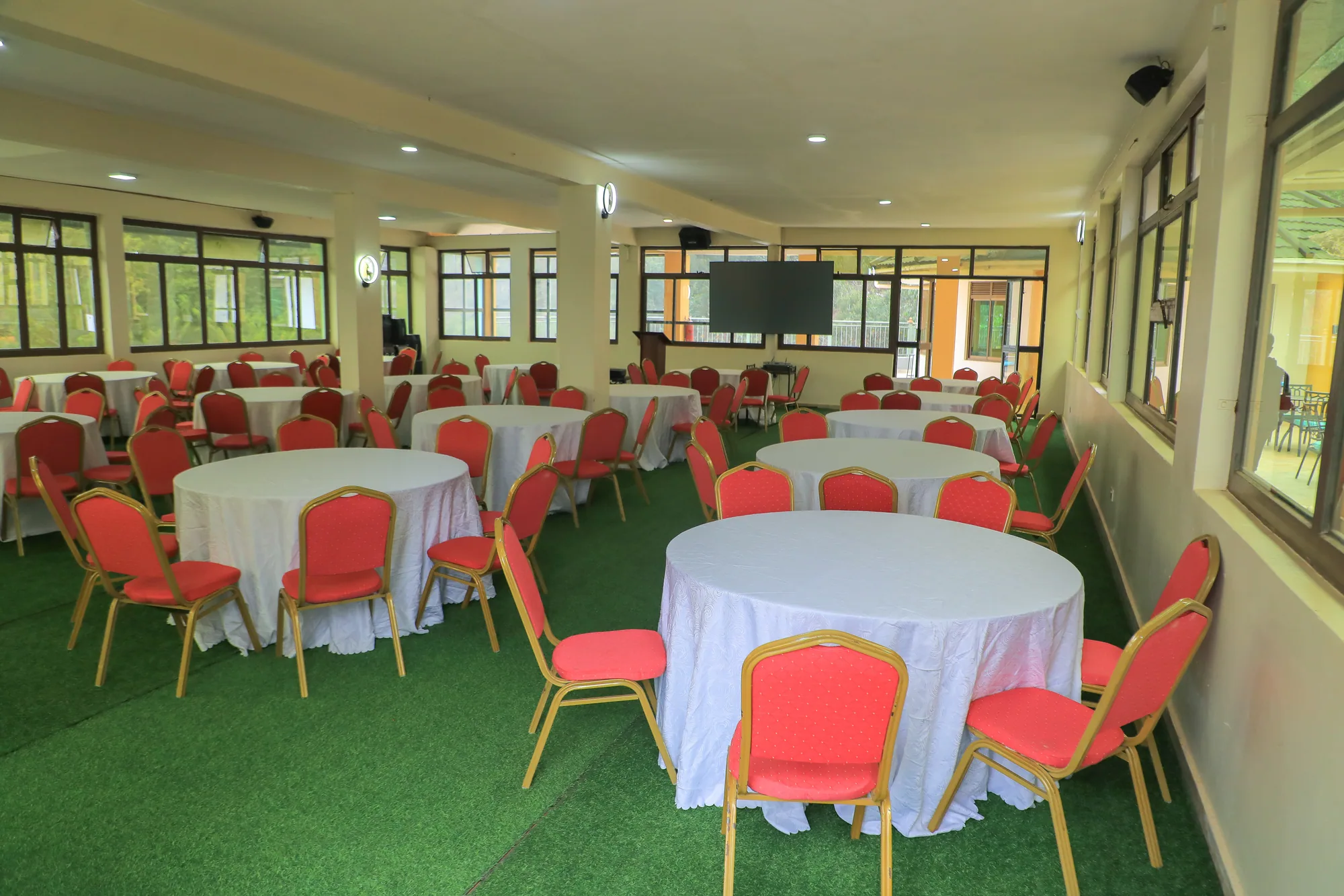 Round banquet tables and red chairs in the events hall, with a wall-mounted screen